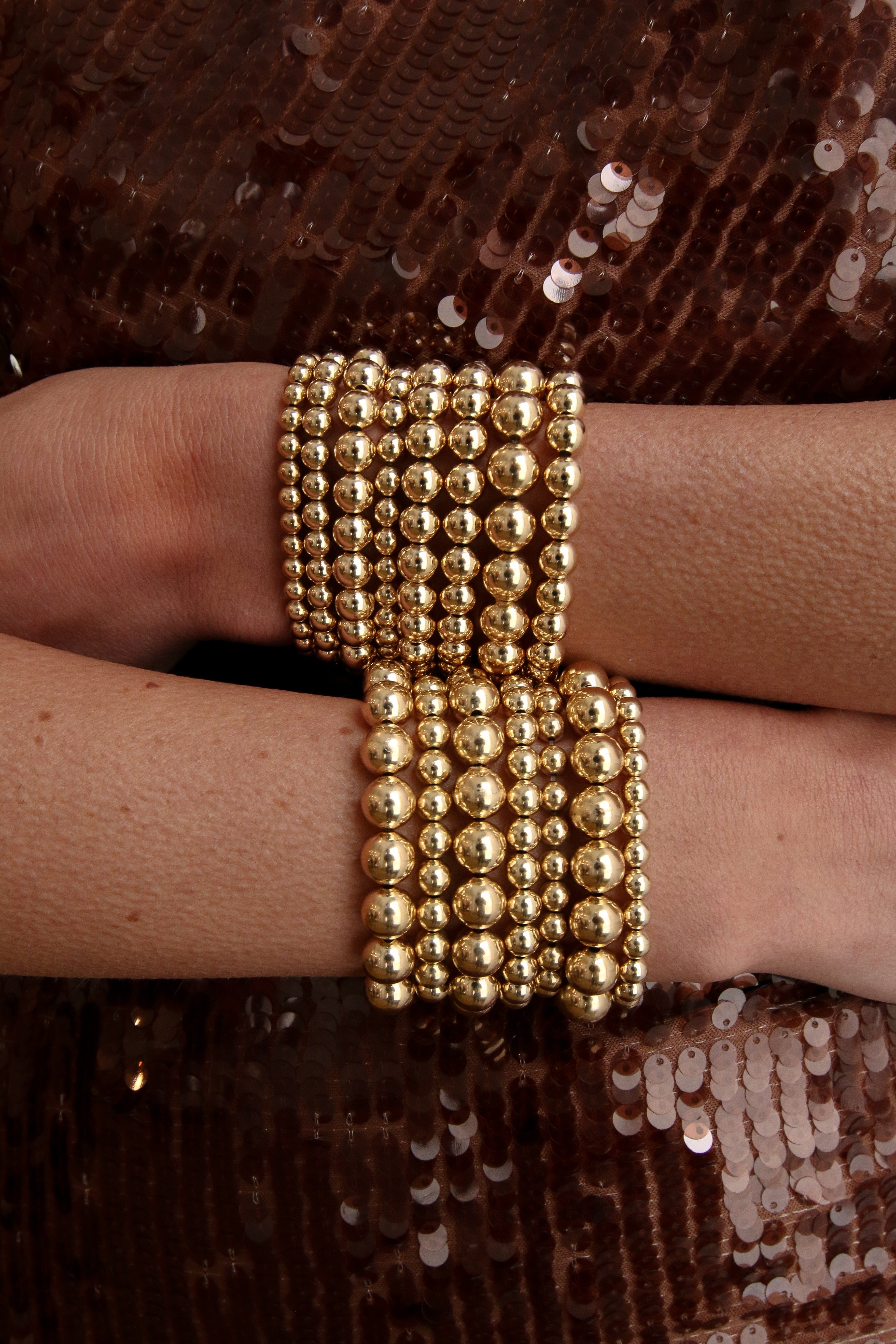Gold beaded bracelet with multiple strands of 4mm spherical beads worn on wrist.