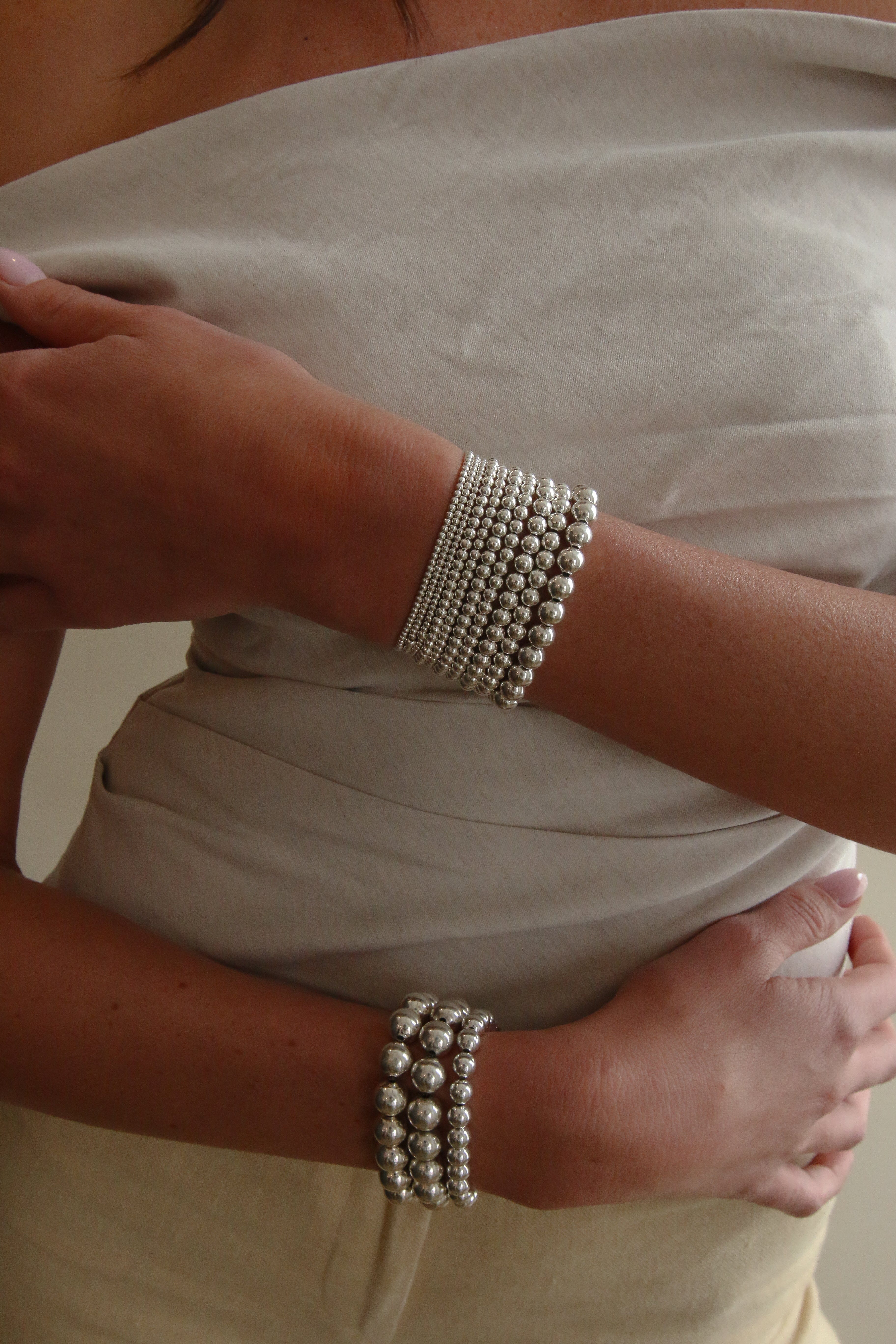 Silver beaded bracelet worn on wrist, composed of multiple strands of small round beads in a stretchy band.