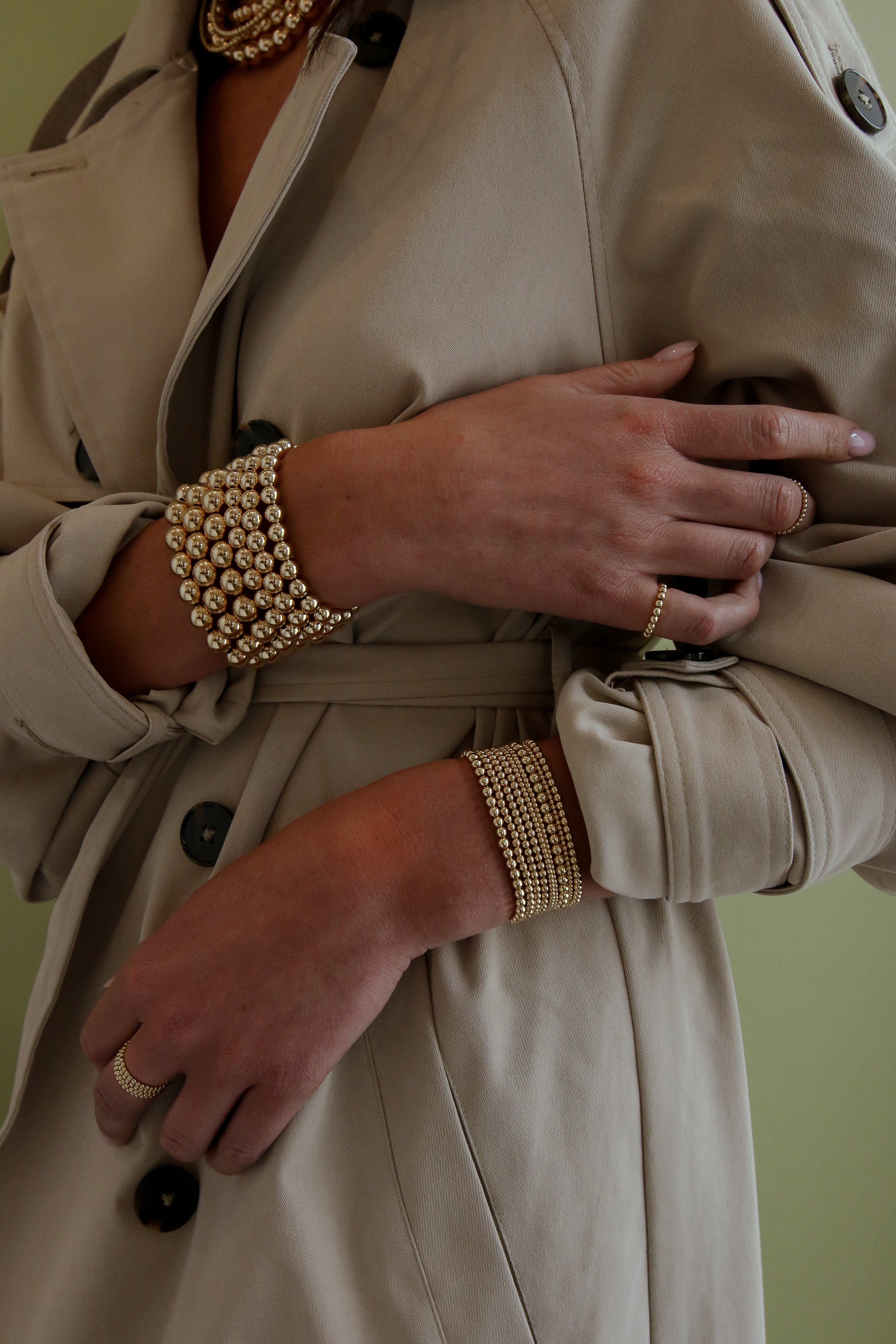 Gold-toned beaded bracelet with small spheres worn on wrist over beige blazer.