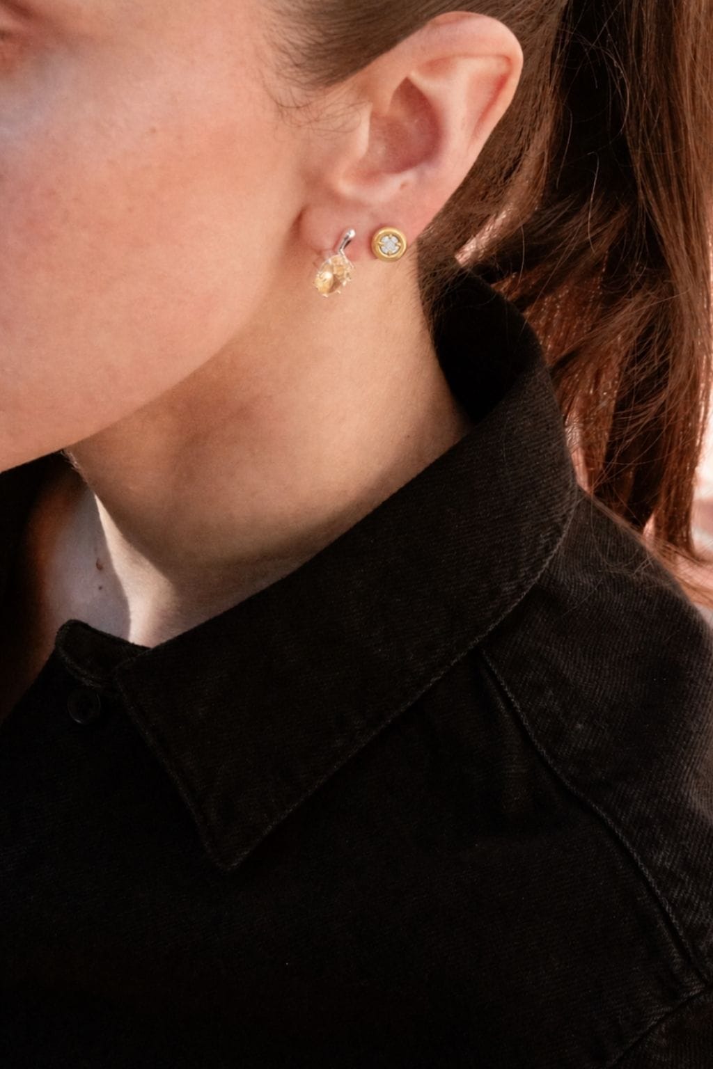 Pair of small gold-toned earrings with crystal stones, one stud and one drop style, worn on ear lobe.