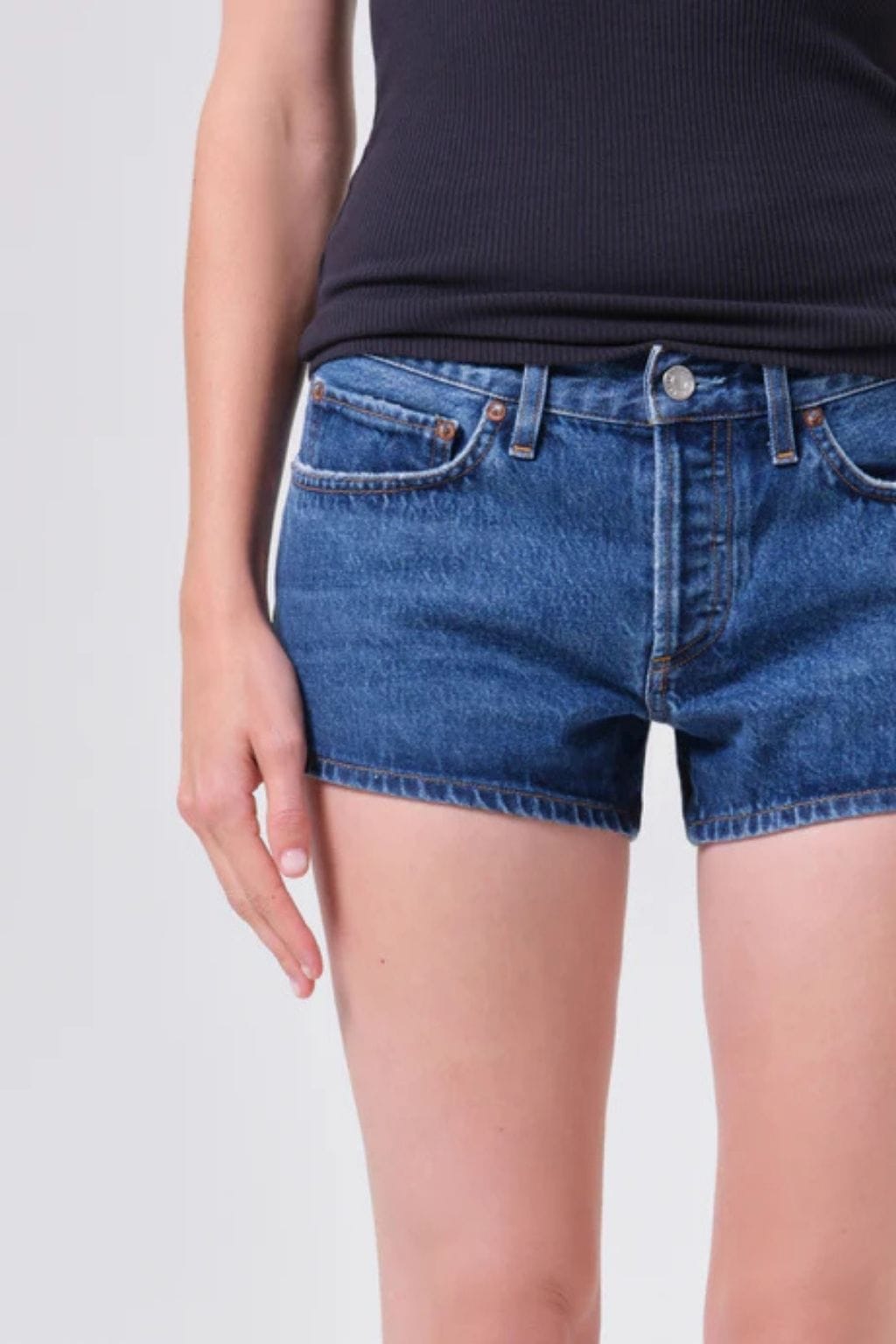 Blue denim low-rise shorts with front pockets and button closure, worn with black ribbed tank top.