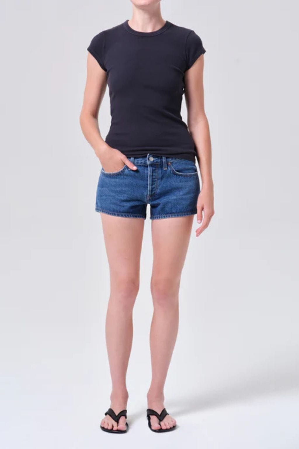 Woman wearing navy cap-sleeve t-shirt and blue denim low-rise shorts with front pockets.