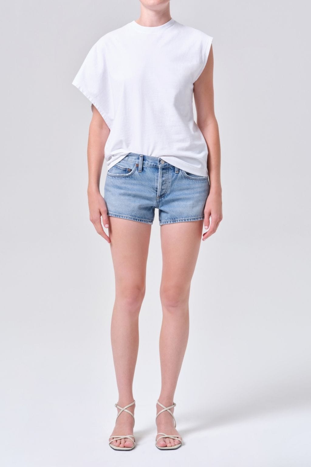 Person wearing light blue denim shorts with a white sleeveless t-shirt and white strappy sandals.