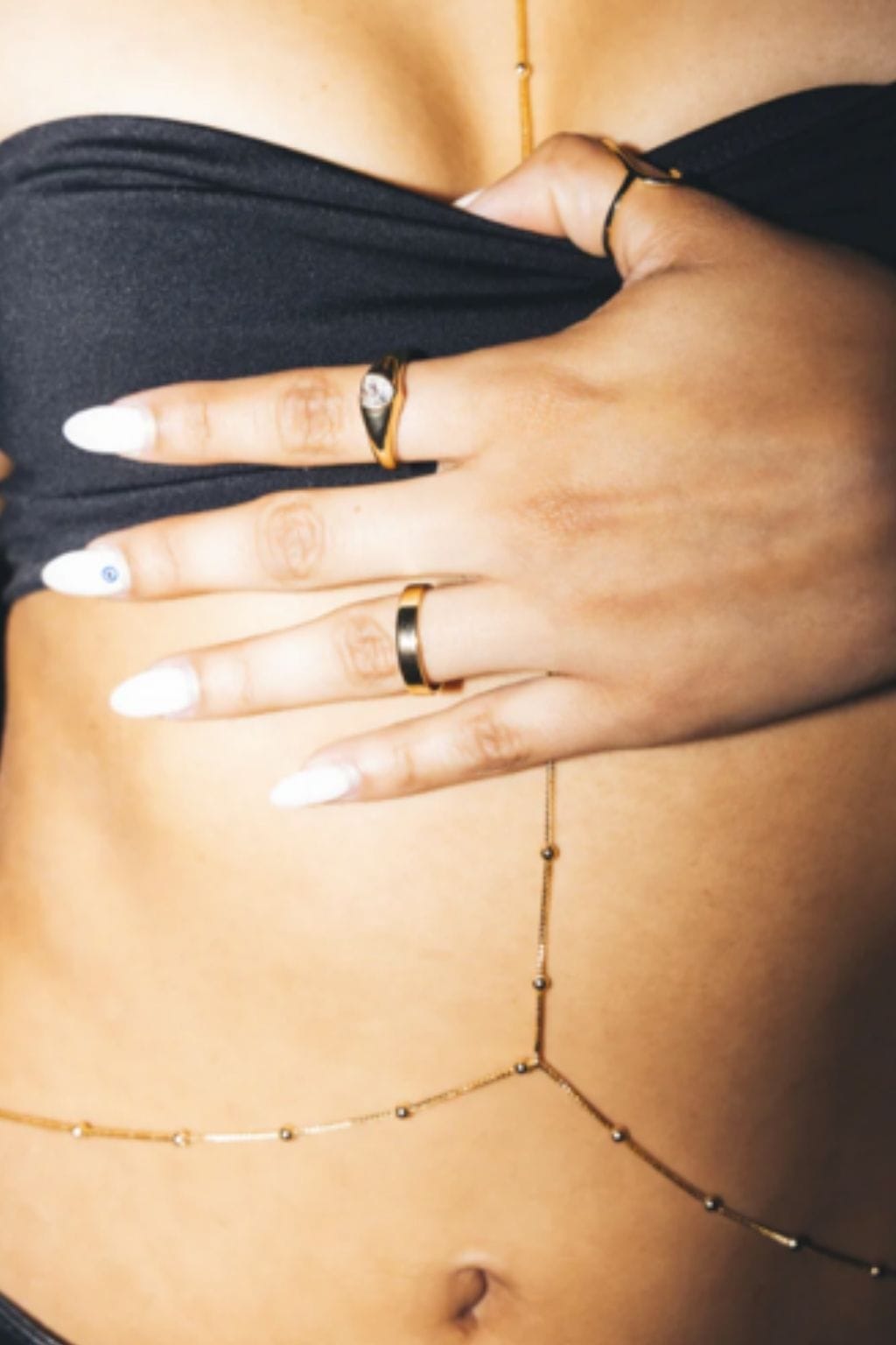 Delicate gold chain body jewelry worn across torso and fingers with small beads, styled on model wearing black clothing.