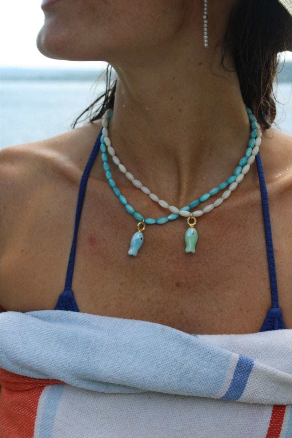 Beaded necklace with turquoise and white oval beads strung on two strands, featuring two small fish-shaped pendants in light 