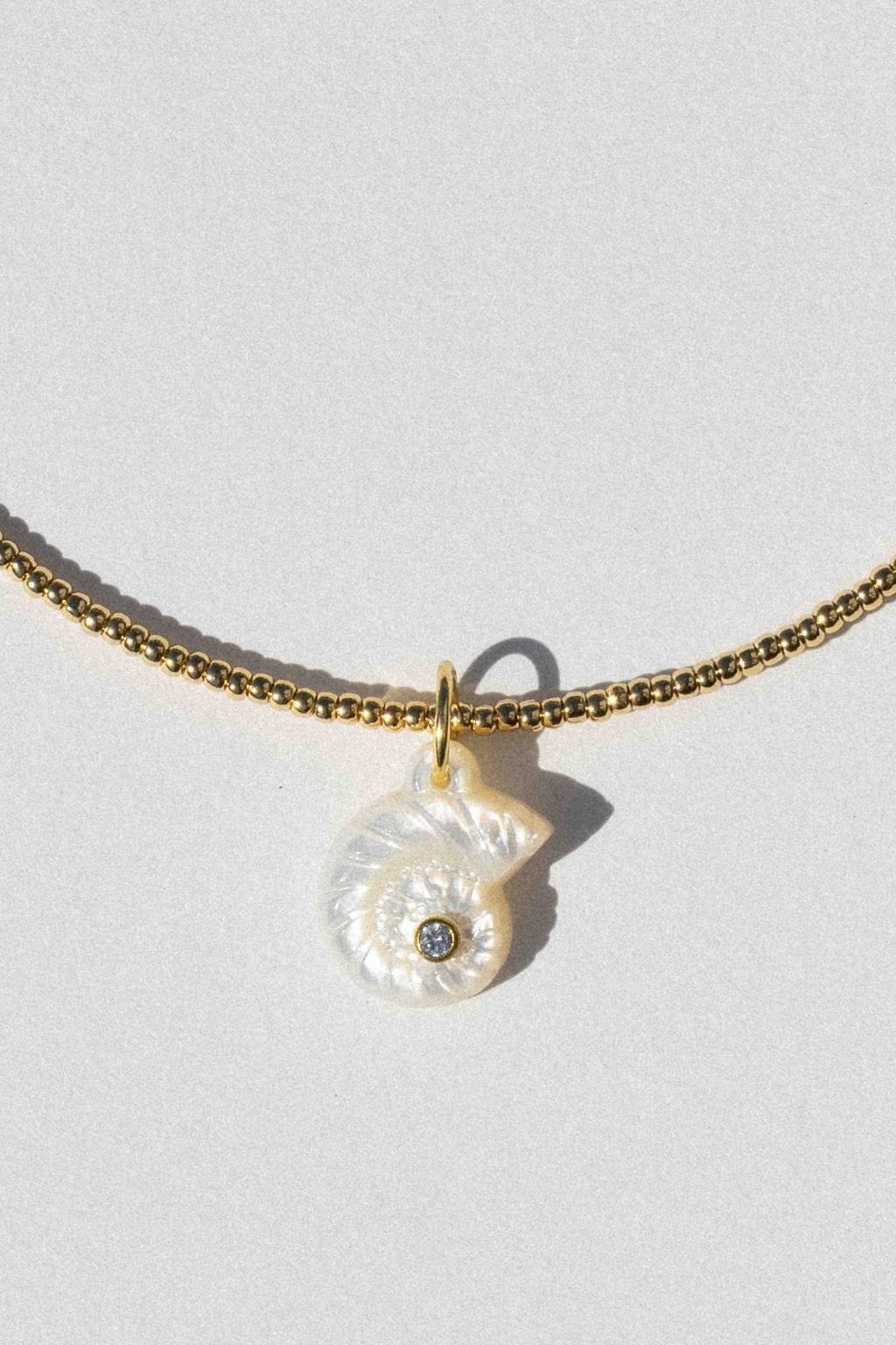 Gold chain collar necklace with white pearl nautilus shell pendant and small stone detail.