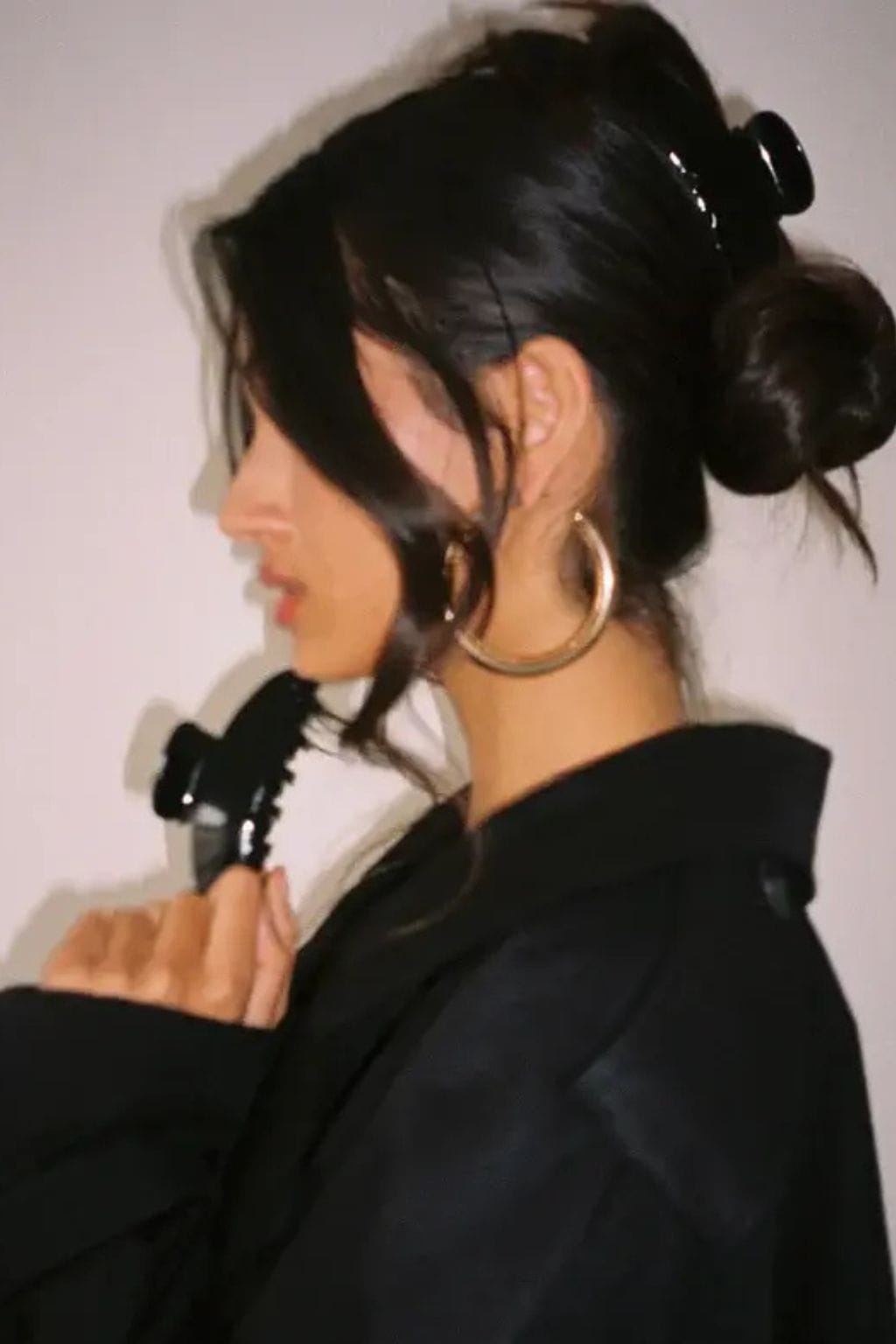 Black hair clip securing dark hair in an updo style on a person wearing a black jacket.