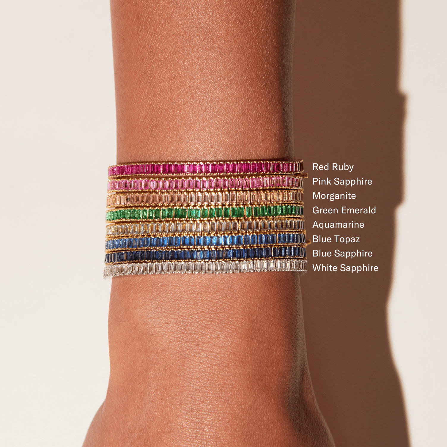 Stack of baguette-cut tennis bracelets in various colors including red, pink, green, blue, and white stones set in metal.