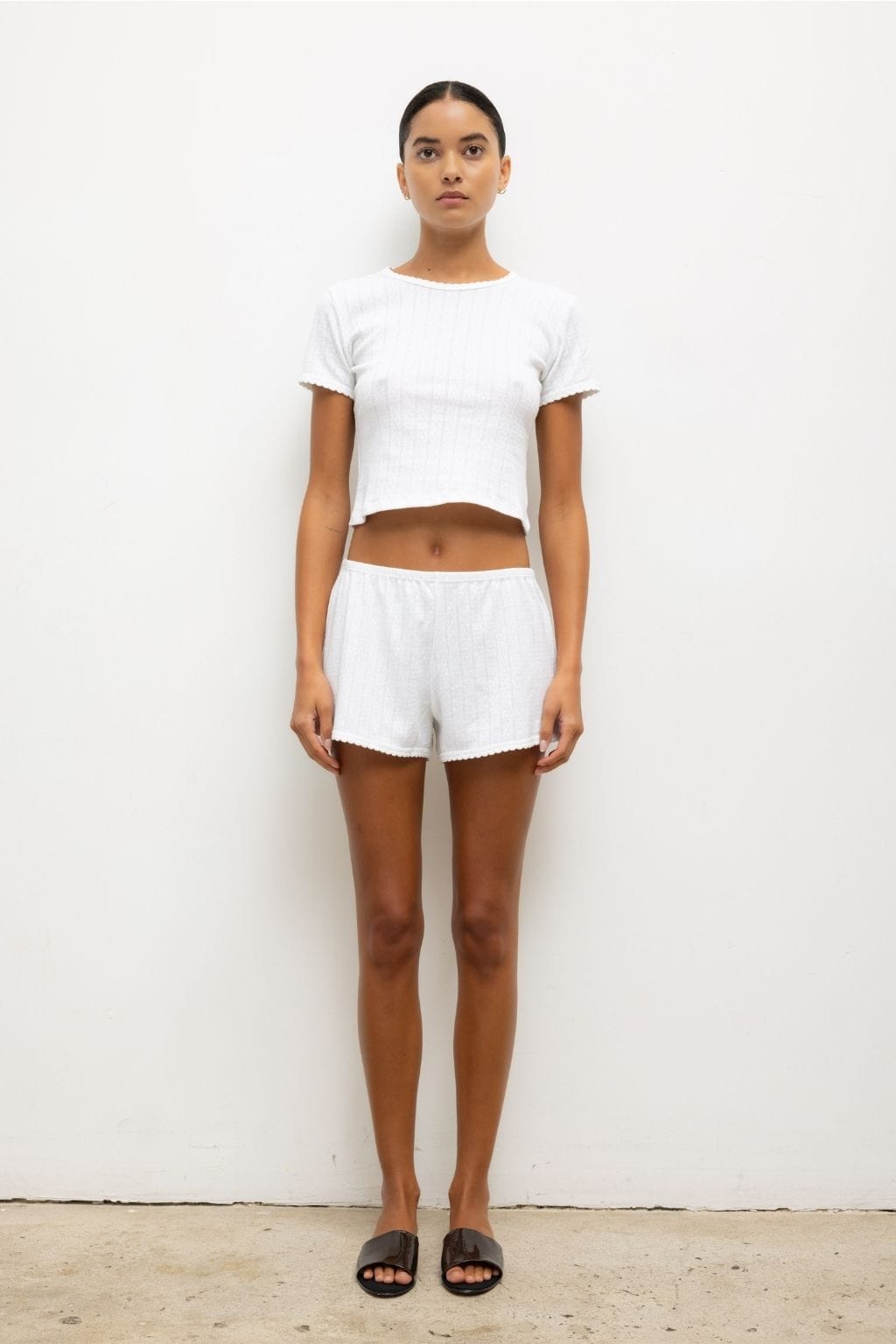 White pointelle mini shorts with elastic waist and scalloped edges, worn with matching crop top.