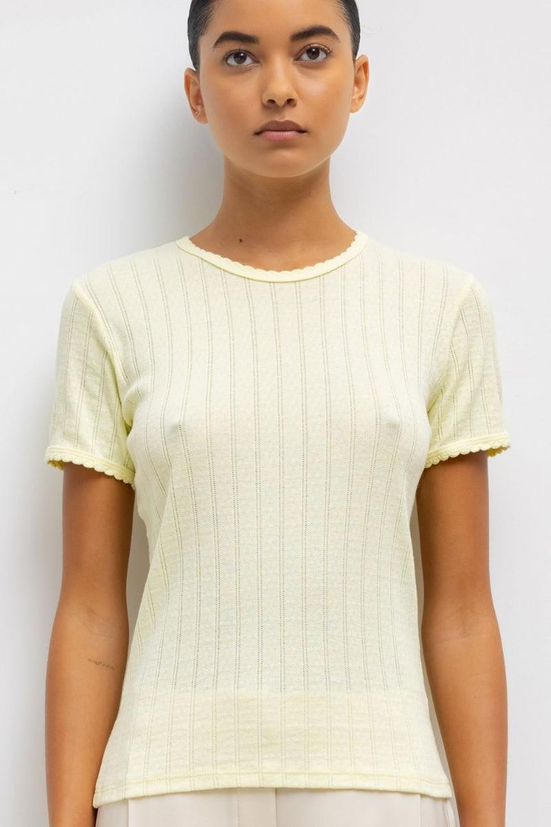 Pale yellow pointelle knit tee with short sleeves and scalloped trim, shown on a model.