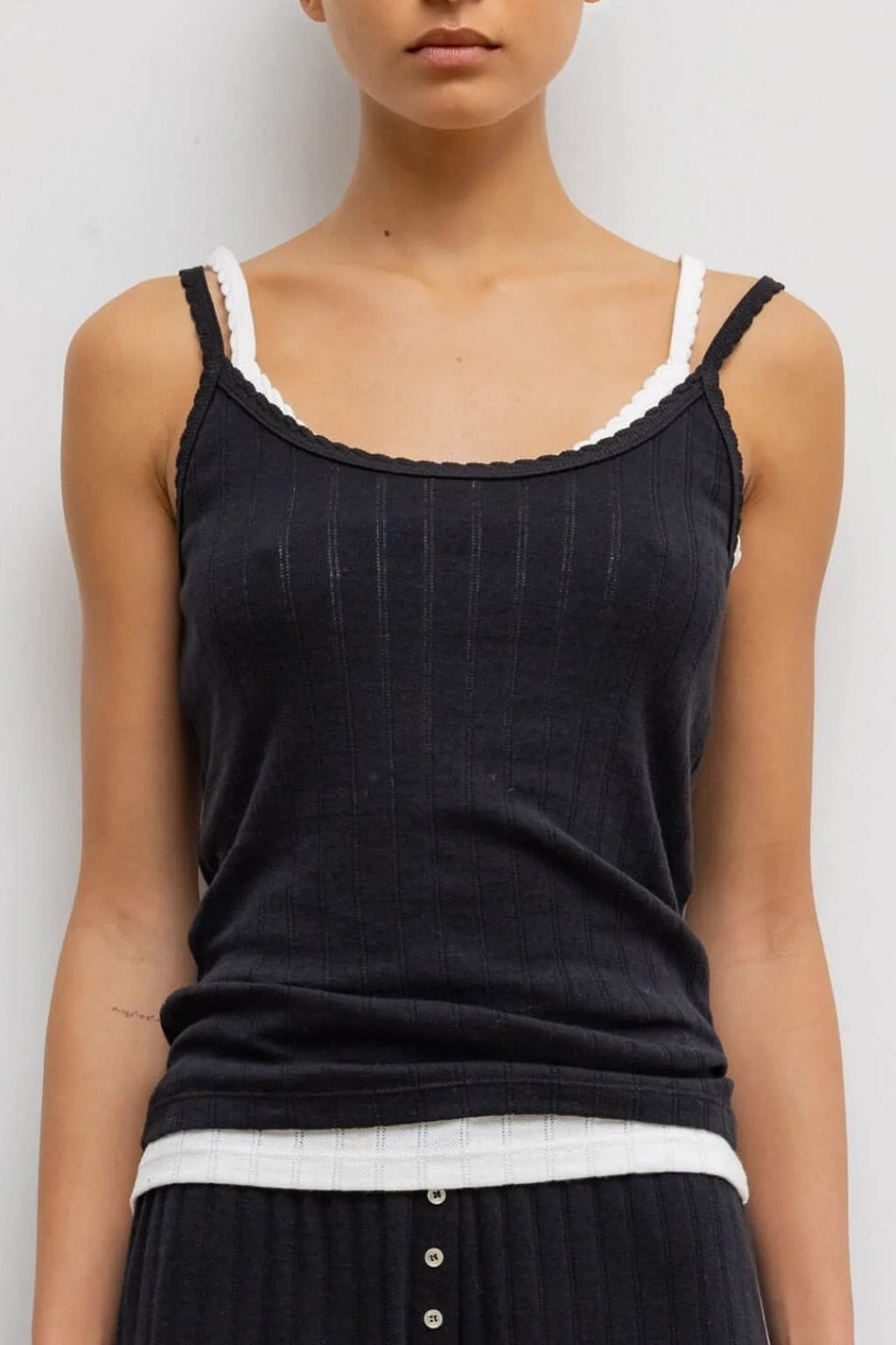 Black pointelle tank top with white trim straps and neckline, displayed on a model.
