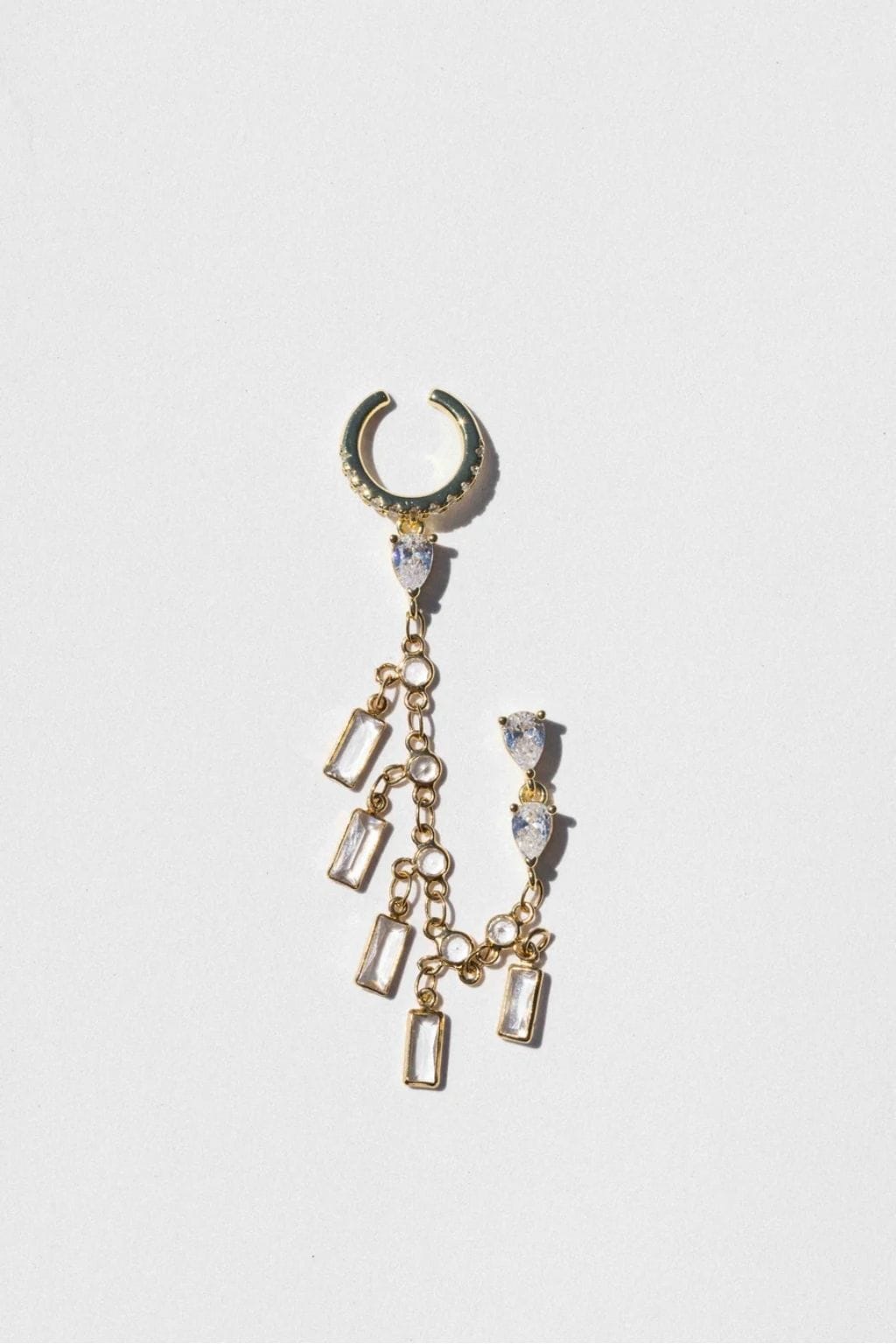 Gold ear cuff with curved top studded with crystals and dangling chain with rectangular and teardrop crystal charms.