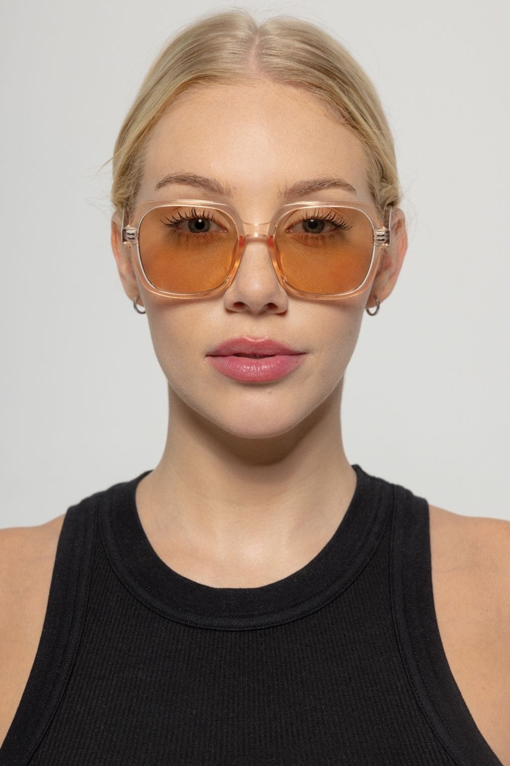 Clear acetate square sunglasses with translucent brown lenses and gold-toned hardware on a model wearing a black tank top.