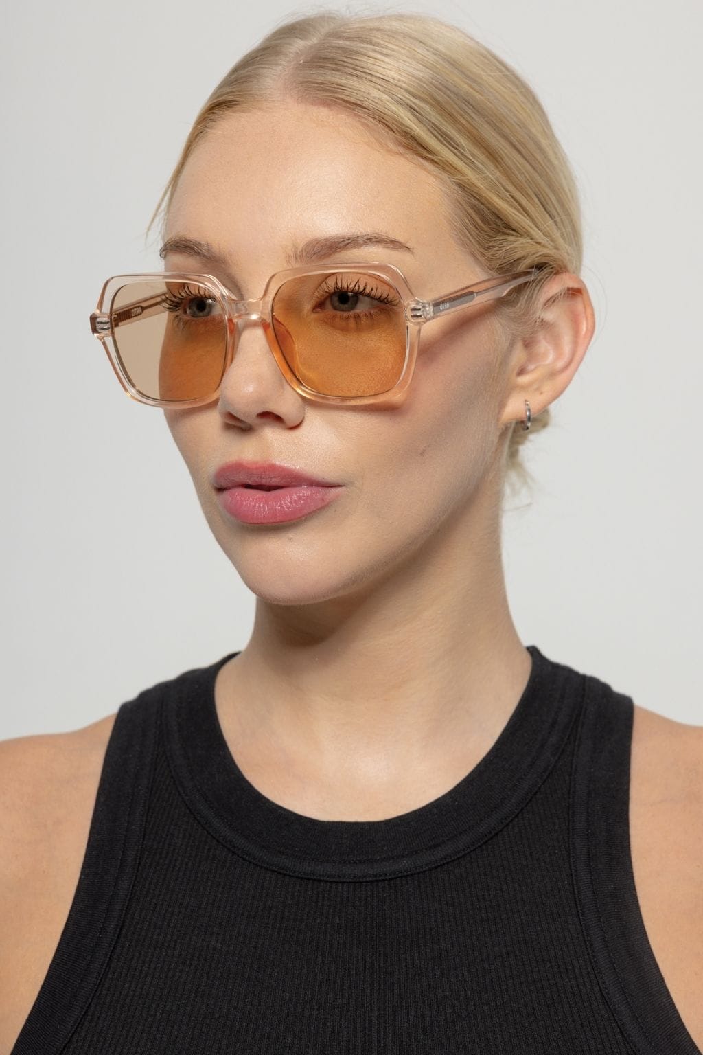 Square-framed sunglasses with translucent brown frames and amber-tinted lenses worn by a person with blonde hair.