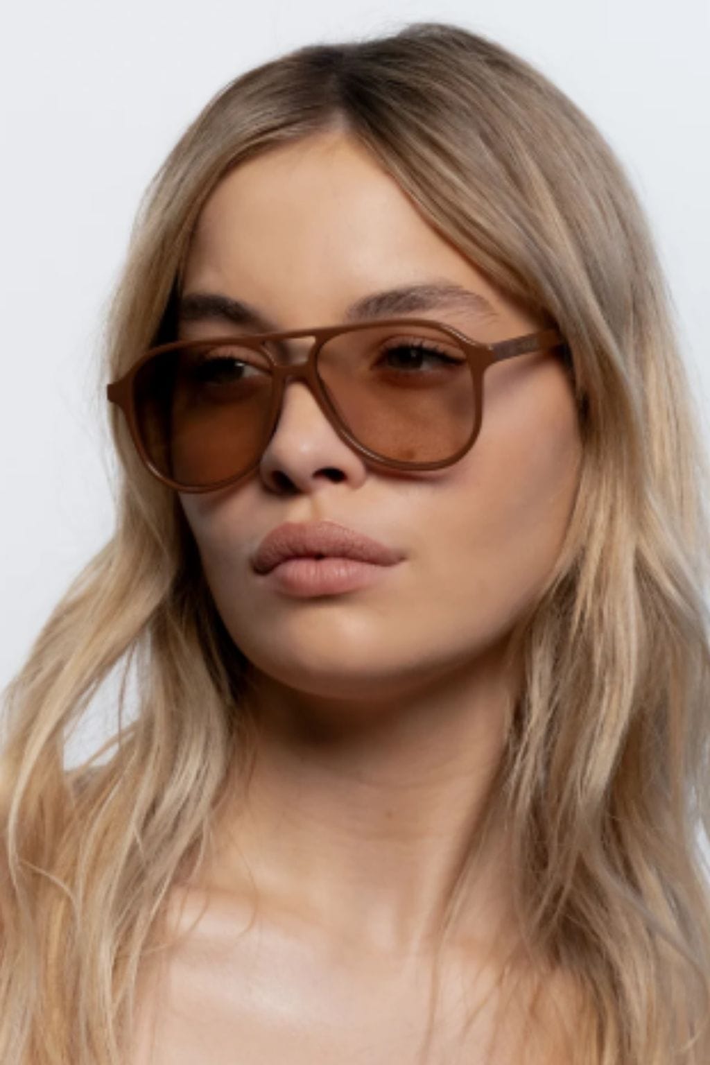 Cinnamon-brown oversized square frame sunglasses worn by person with long blonde hair.
