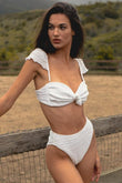 White textured bikini top with ruched sweetheart neckline and adjustable shoulder straps on model outdoors.