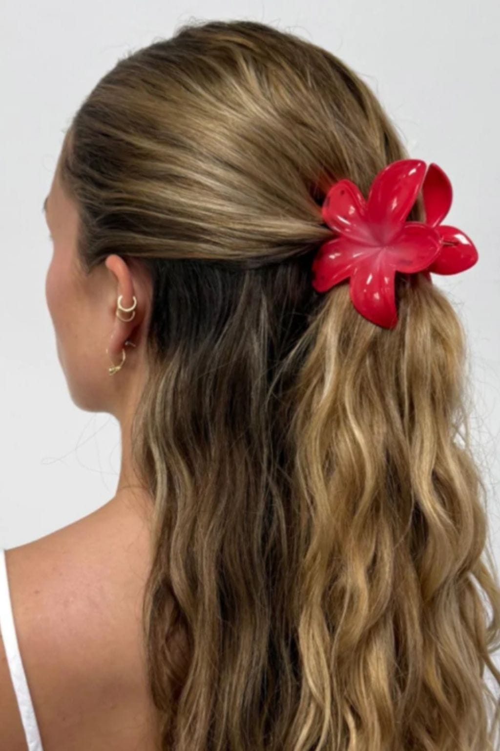 Red flower-shaped hair clip worn in long, layered blonde hair on the back of the head.