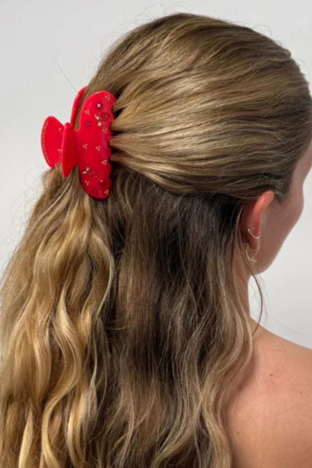 Red heart-shaped hair clip with glitter detail worn in long brown hair.