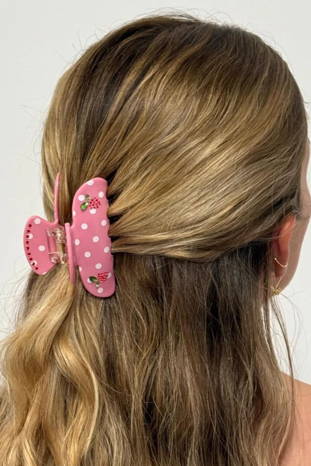 Pink hair clip with white polka dots and floral embellishment, clipped in shoulder-length brown hair.