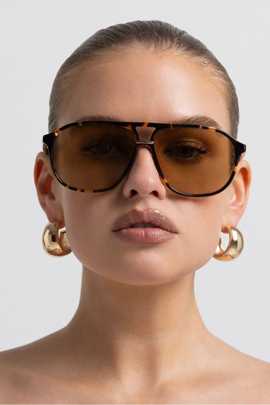 Amber tortoise aviator sunglasses with brown tinted lenses worn by a person against a white background.