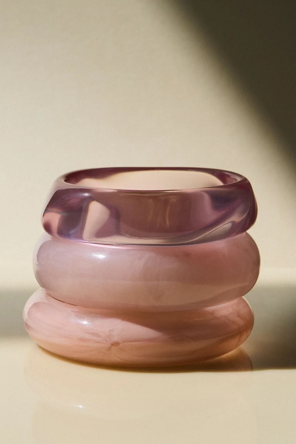 Three stacked pink resin bangles with varying translucent tones, displayed against a neutral background.