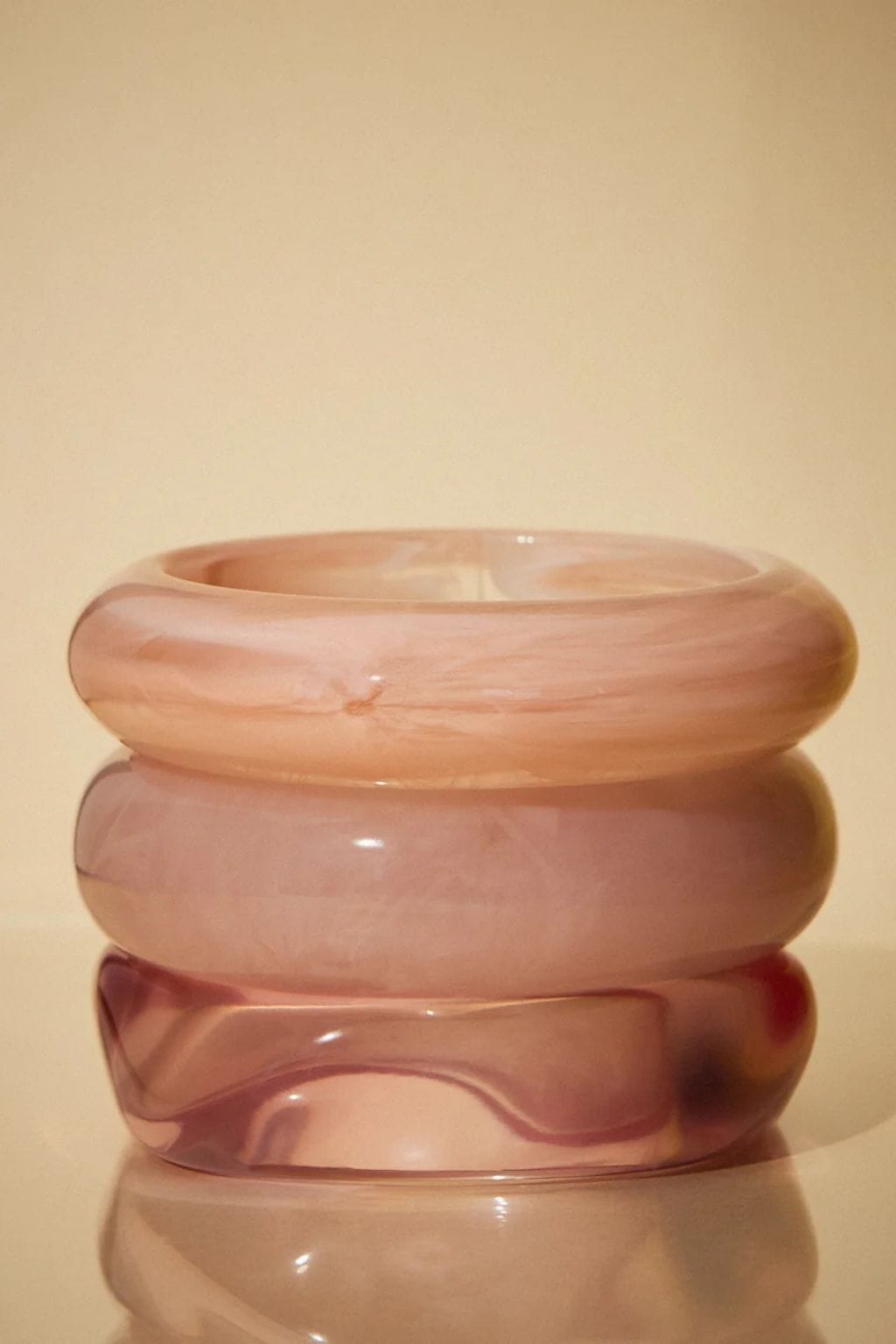 Three stacked pink resin bangles in varying shades, displaying smooth polished finishes and organic curved designs.