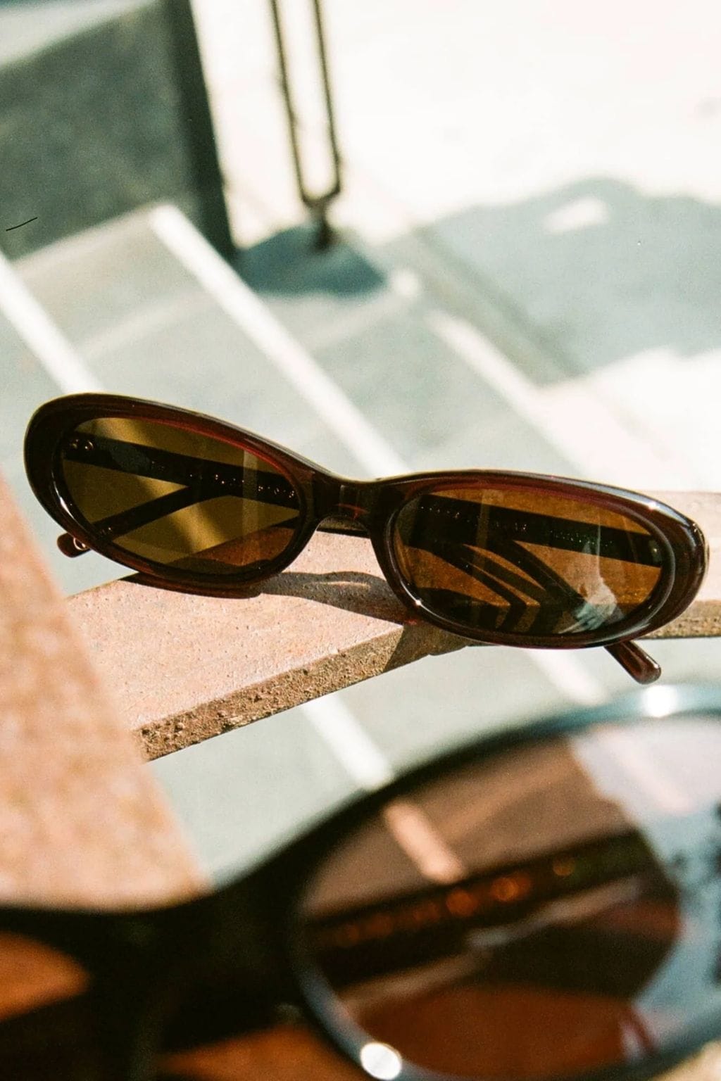 Tortoiseshell oval sunglasses with brown tinted lenses resting on a beige surface.