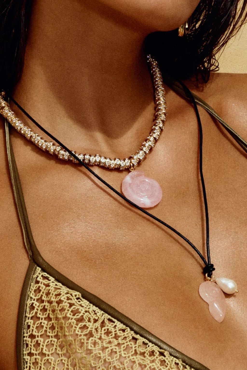 Black cord necklace with pale pink stone pendant and pearl accent, worn layered with rhinestone necklace.