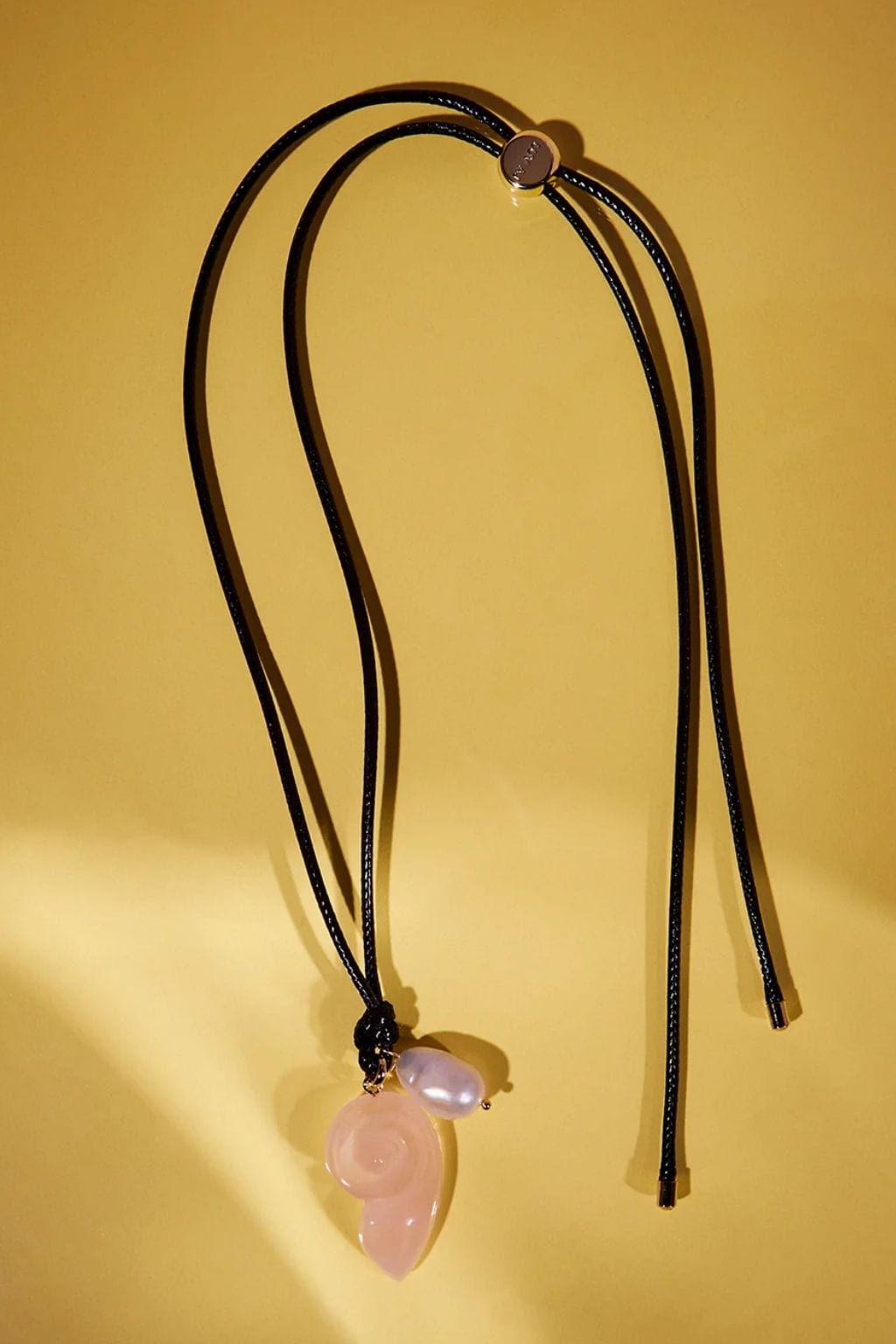 Black cord necklace with pink stone leaf pendant and small bead detail.