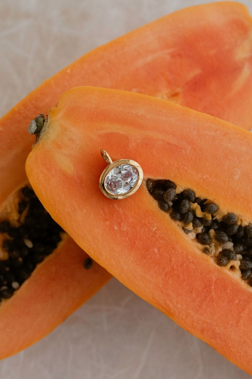 Round diamond charm with bezel setting and loop attachment on papaya fruit.