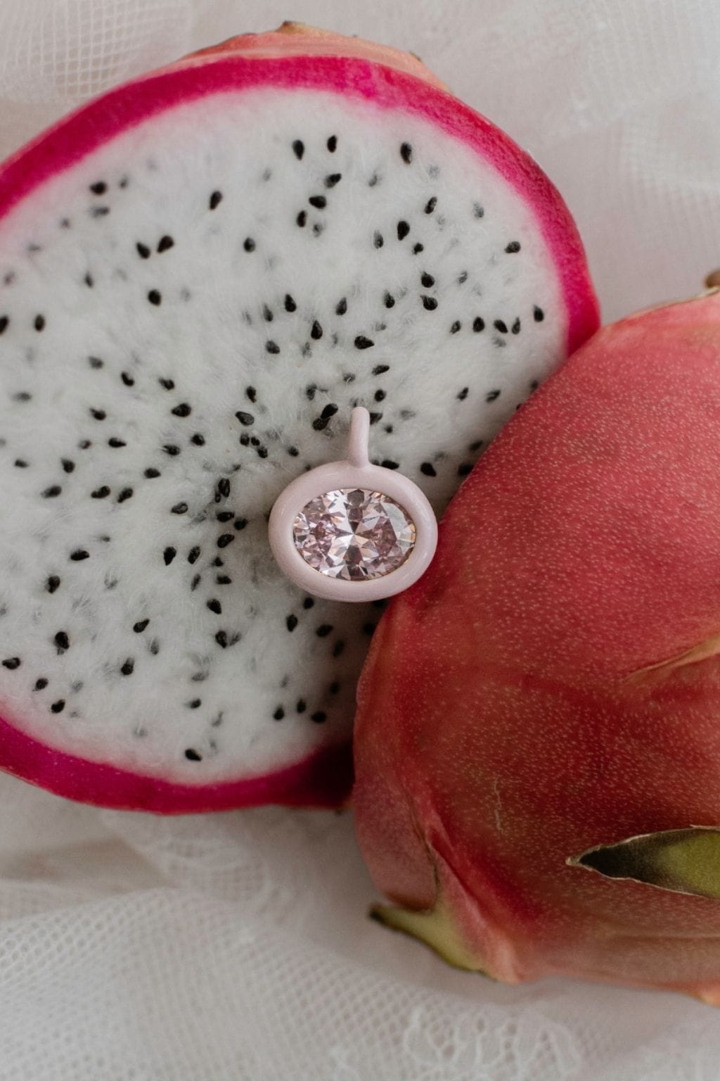 Pink circular charm with faceted crystal center displayed on sliced dragon fruit.