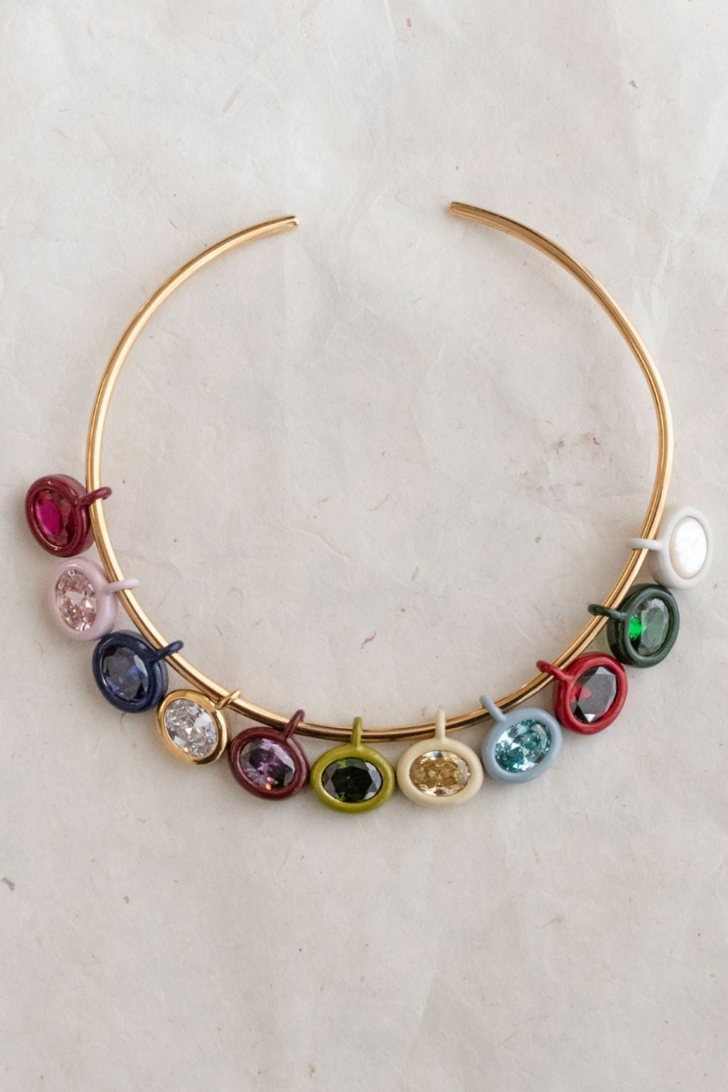 Gold-tone bangle bracelet with multiple colored gemstone charms including ruby, sapphire, and other birthstones in enamel set