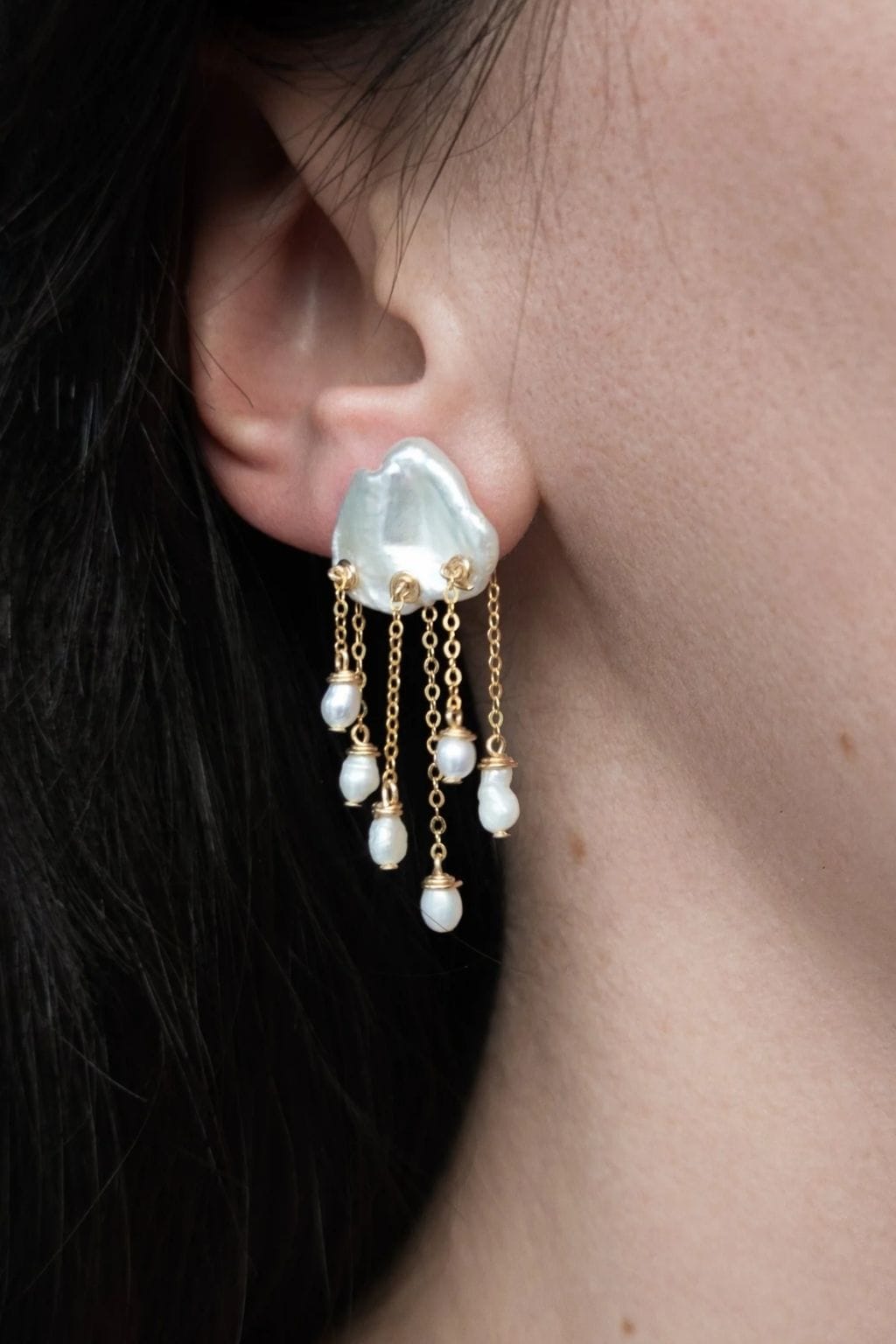 White teardrop earrings with gold chain strands and pearl accents, worn on earlobe.
