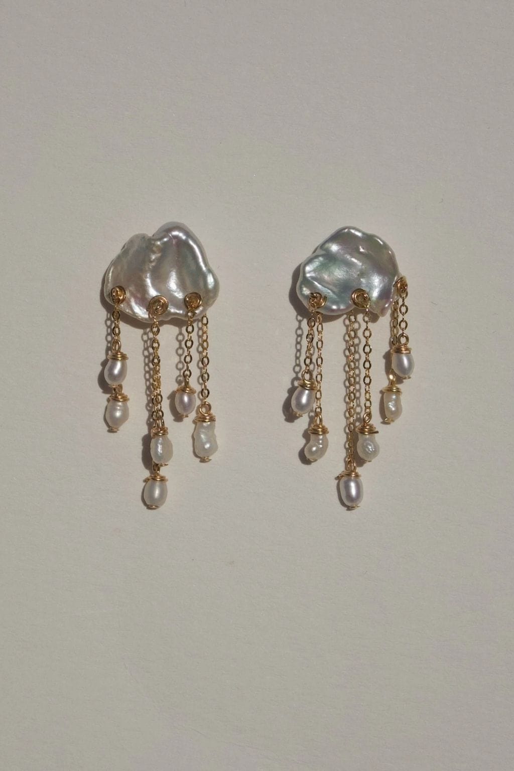 Pair of white pearl drop earrings with iridescent dome tops, gold-tone accents, and multiple dangling pearl strands.