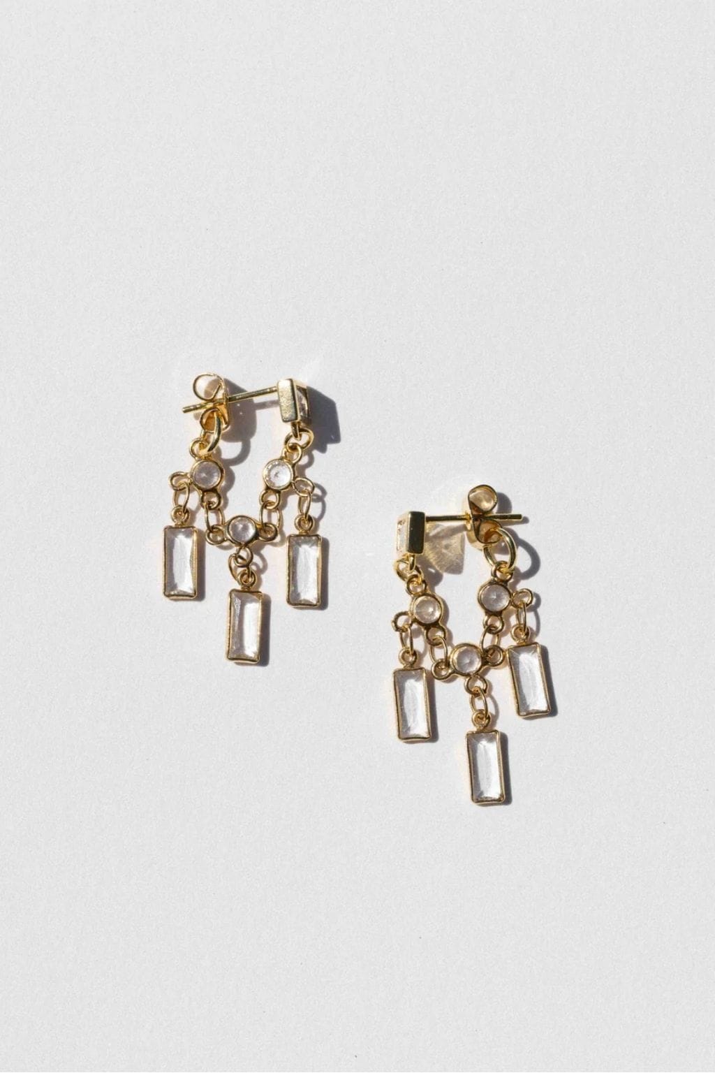 Gold-toned stud earrings with rectangular crystal stones and beaded chain details hanging from the posts.