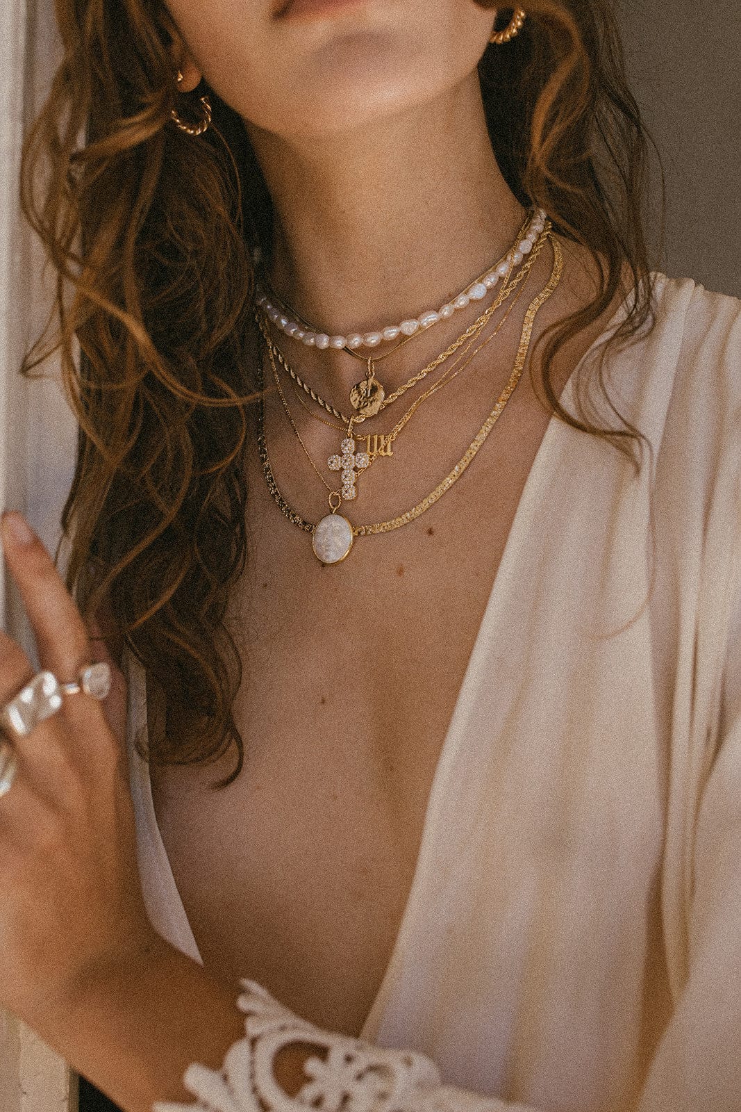 Pearl beaded necklace in gold worn layered with other pendant chains around a woman's neck.