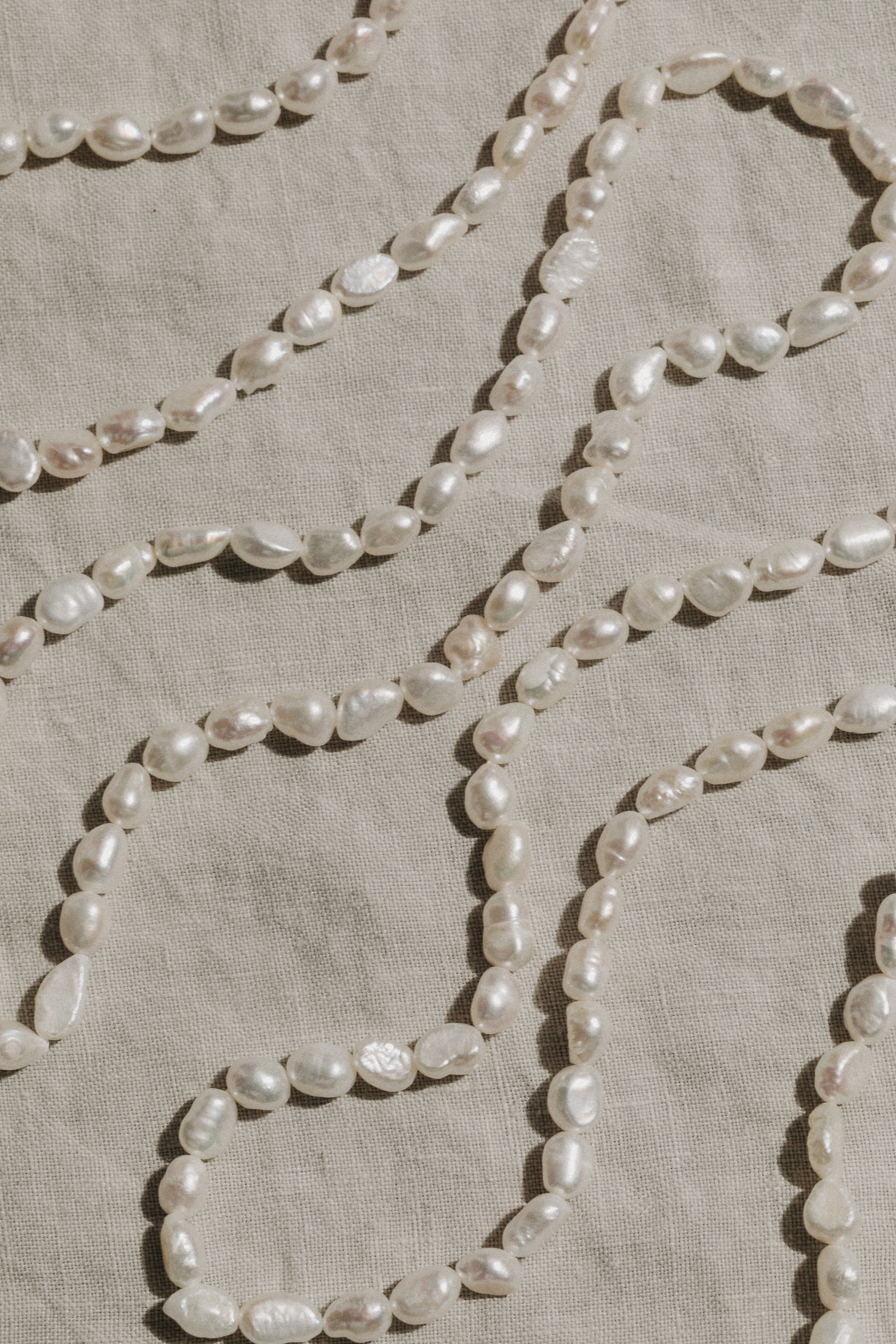 Strands of white baroque pearls arranged in curved rows on a neutral fabric background.