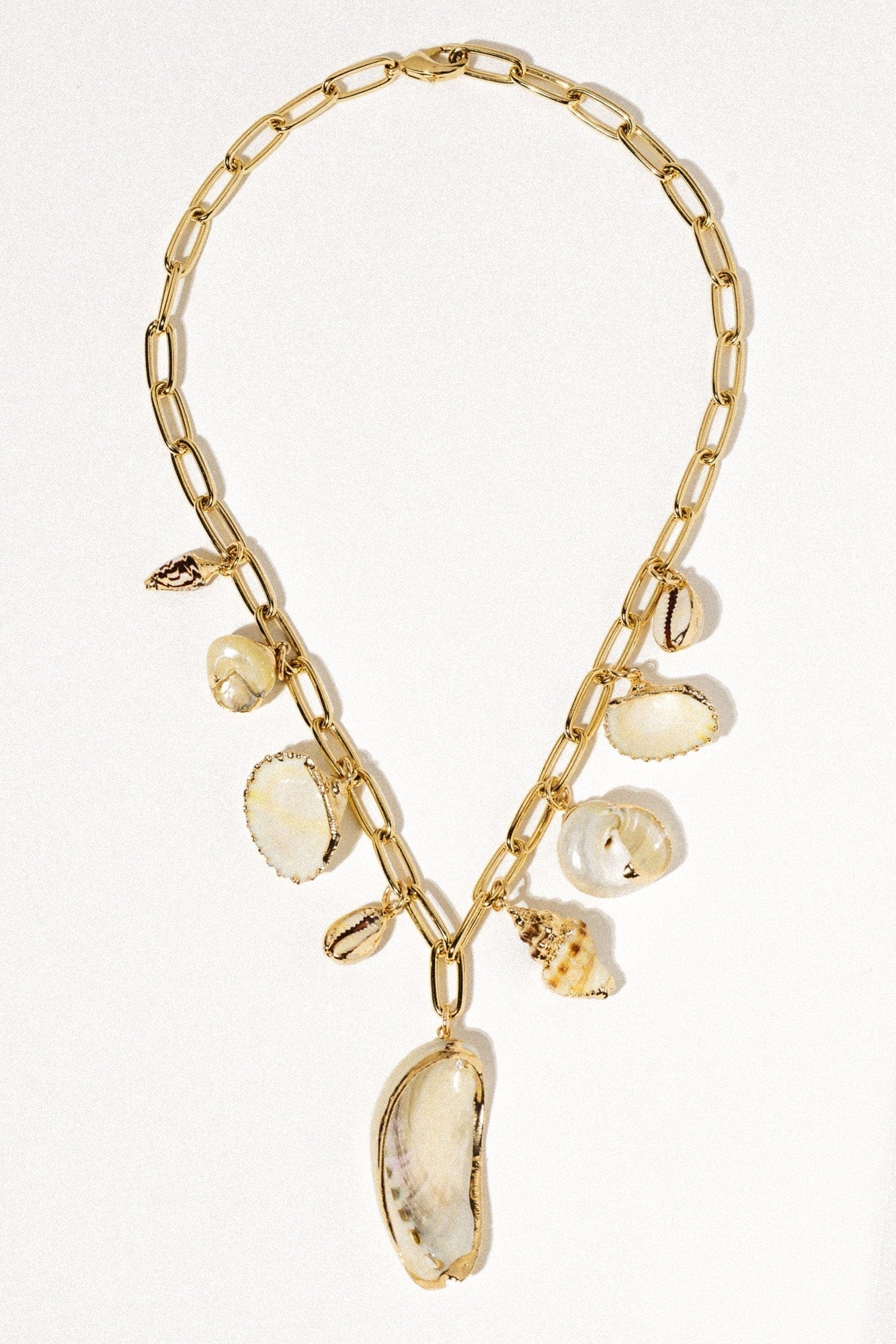 Gold chain necklace with oval and shell-shaped charm pendants in cream and natural tones.