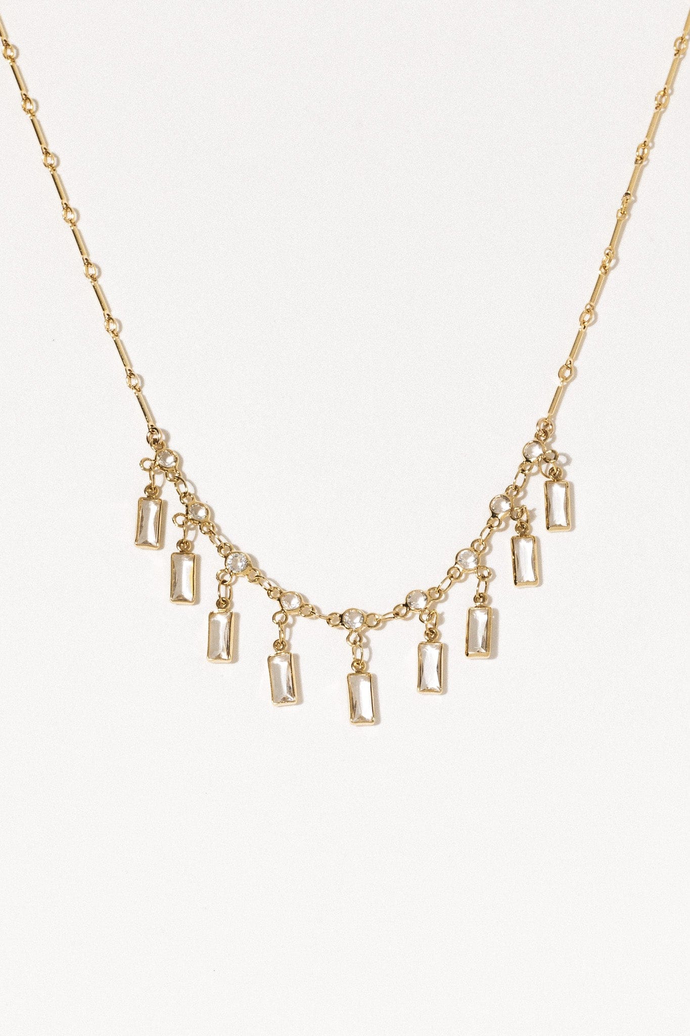 Gold-tone necklace with segmented chain and rectangular crystal pendant drops arranged in a curved pattern.
