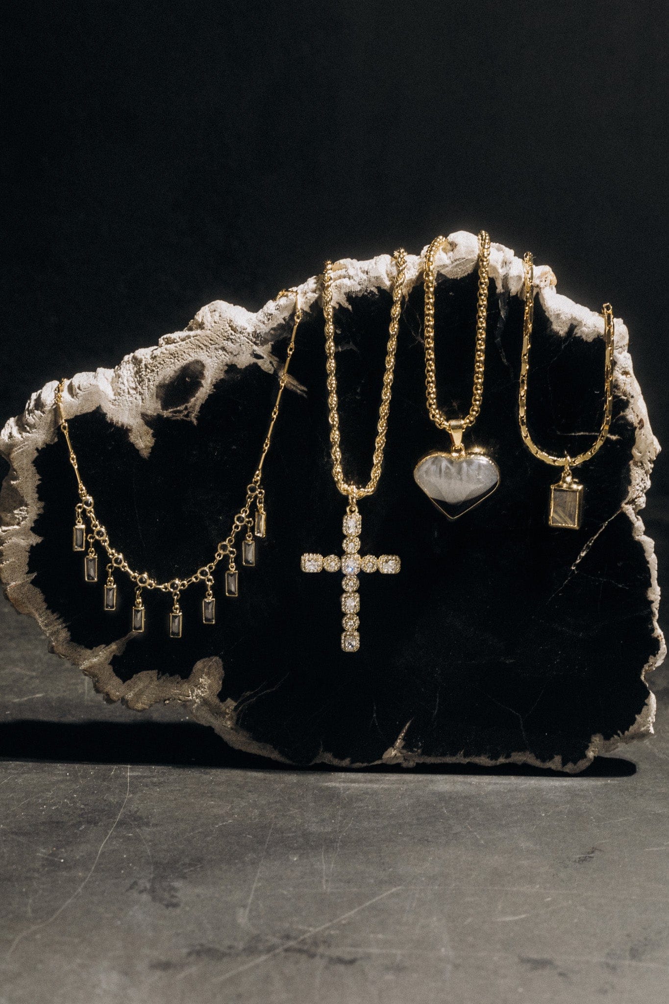 Gold-tone necklaces with cubic zirconia stones displayed on a textured white stone bust, including chains with heart, cross, 