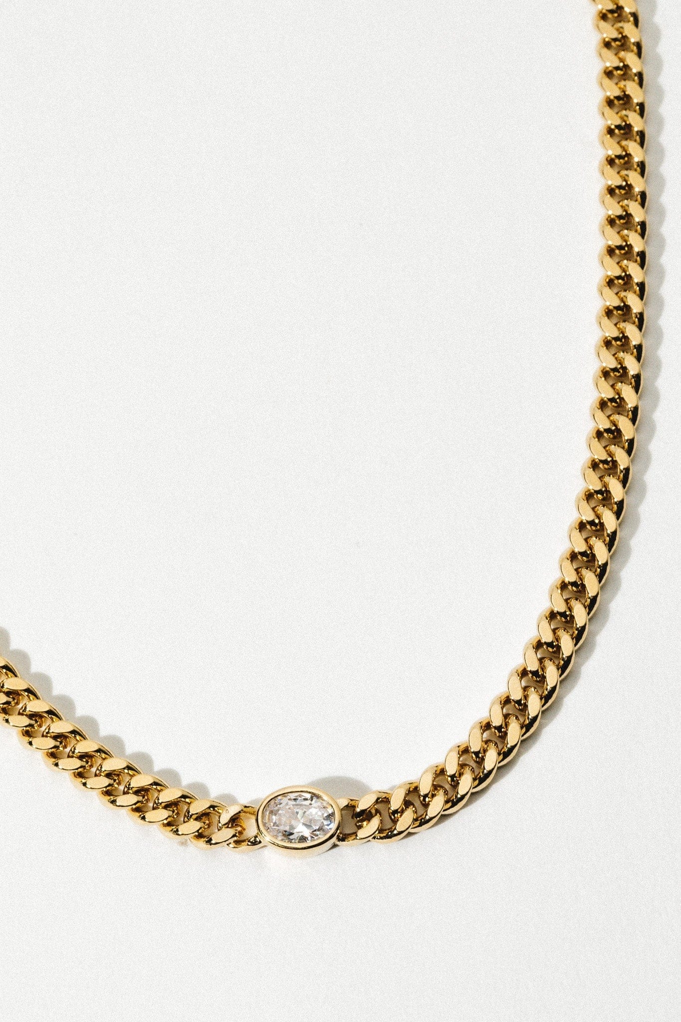 Gold-tone curb chain necklace with oval crystal pendant centerpiece against white background.