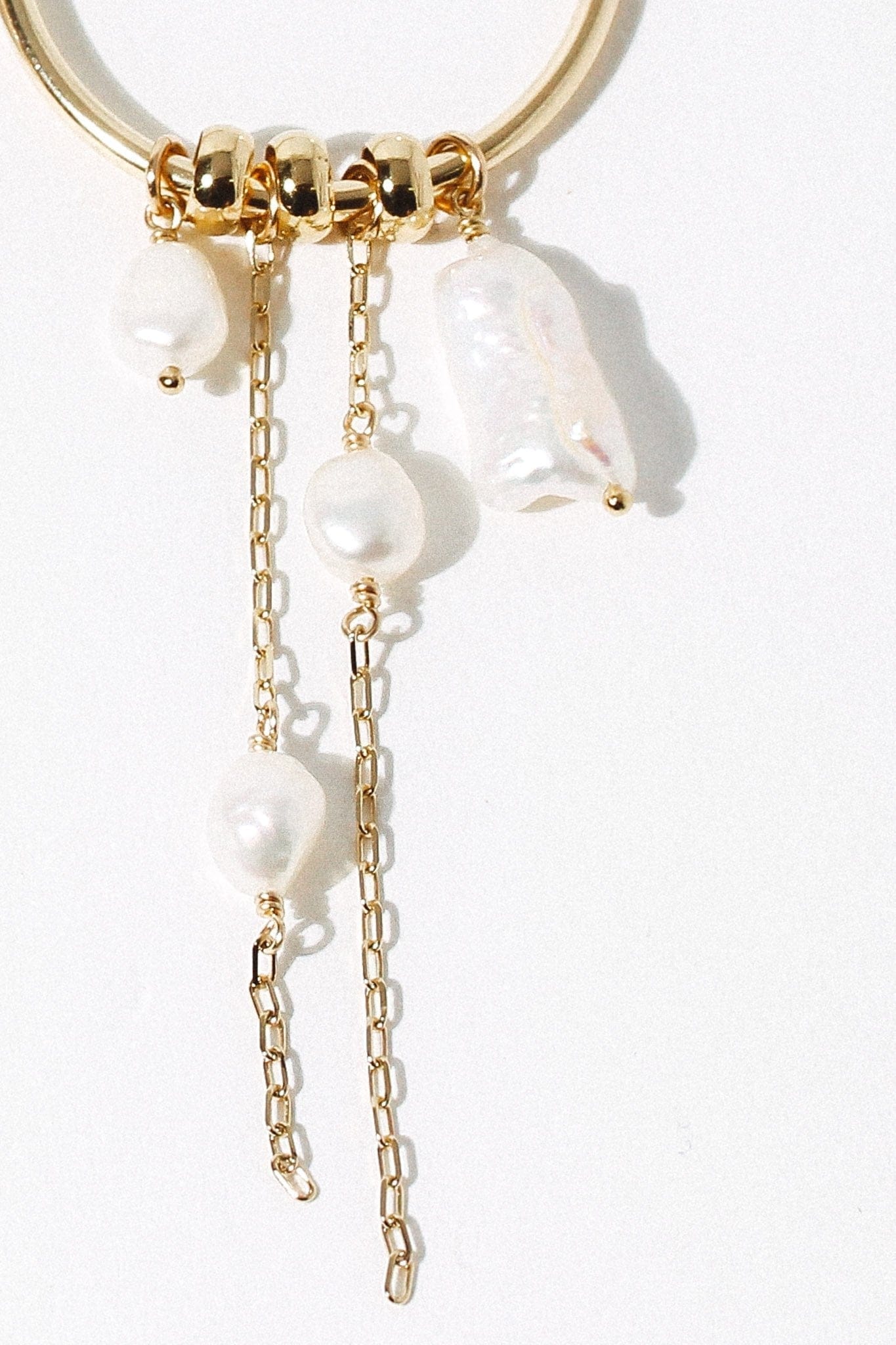 Pair of drop earrings with white baroque pearls and gold-toned chain links attached to gold spacer beads on a curved metal ho