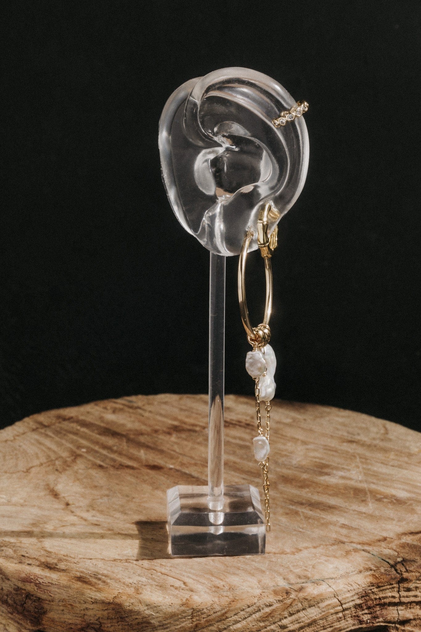Pair of gold-tone hoop earrings with pearl beads displayed on an ear-shaped acrylic stand.