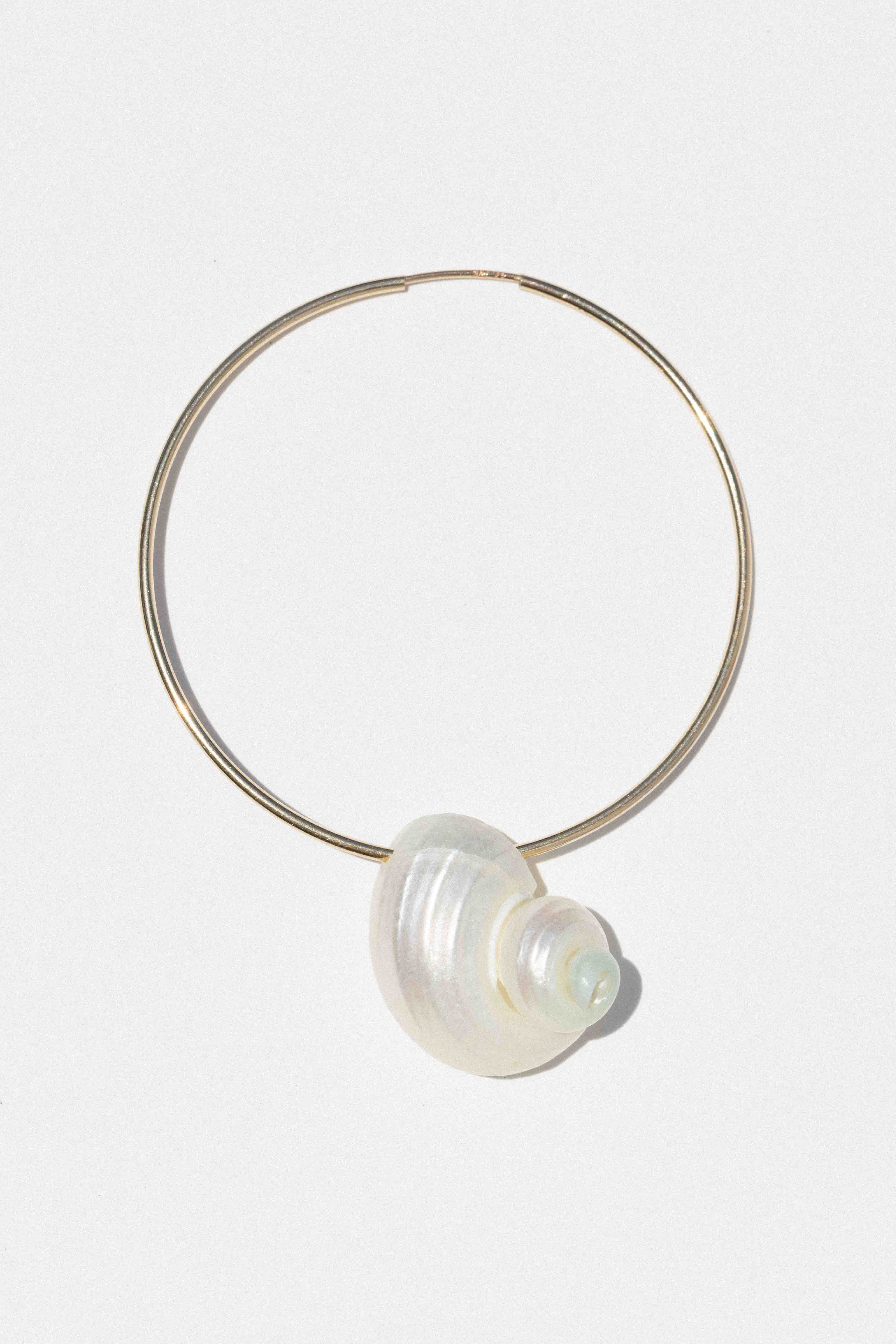 Gold-toned hoop earring with white spiral shell pendant hanging at bottom center.
