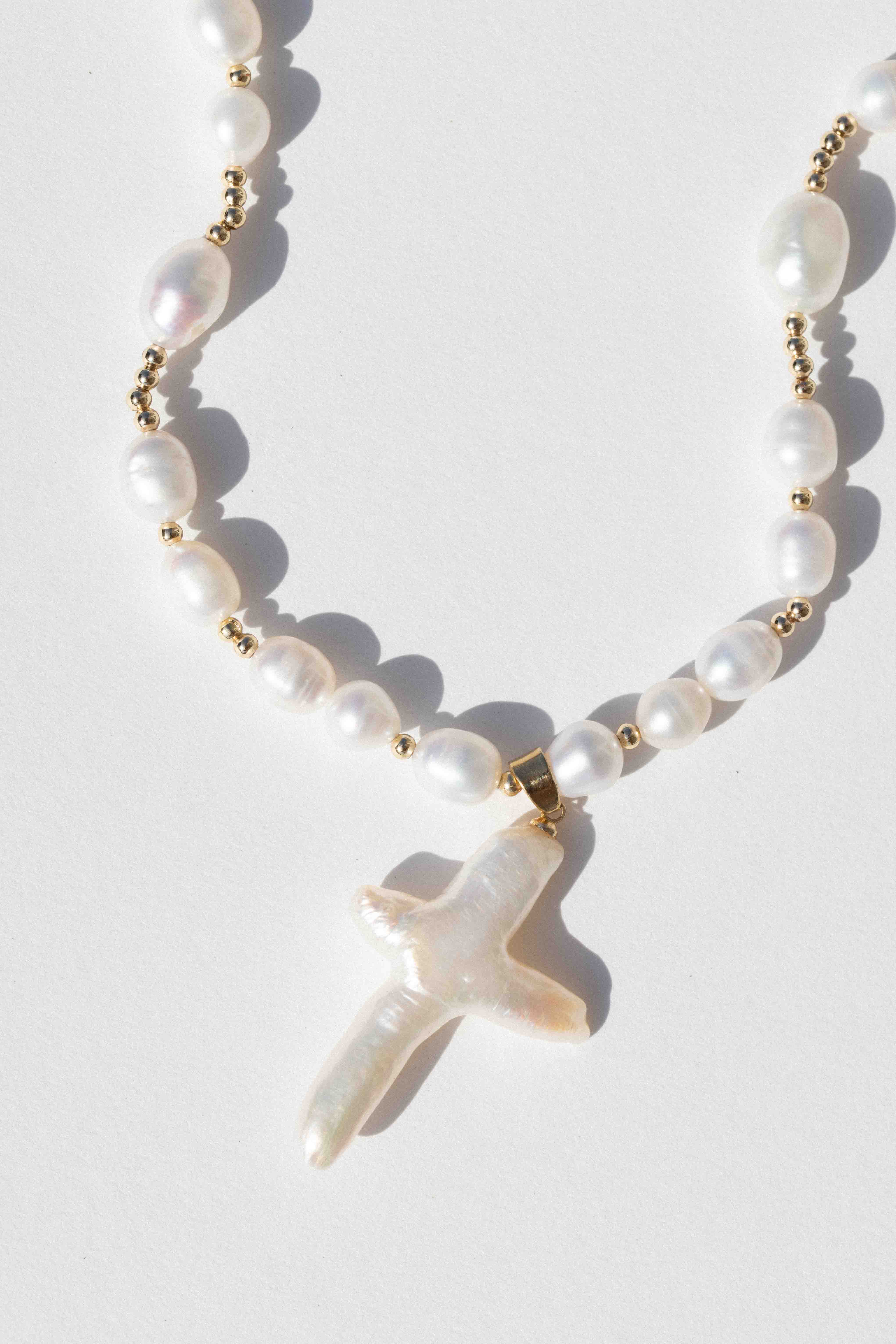 Gold-toned necklace with white pearls and a baroque pearl cross pendant.