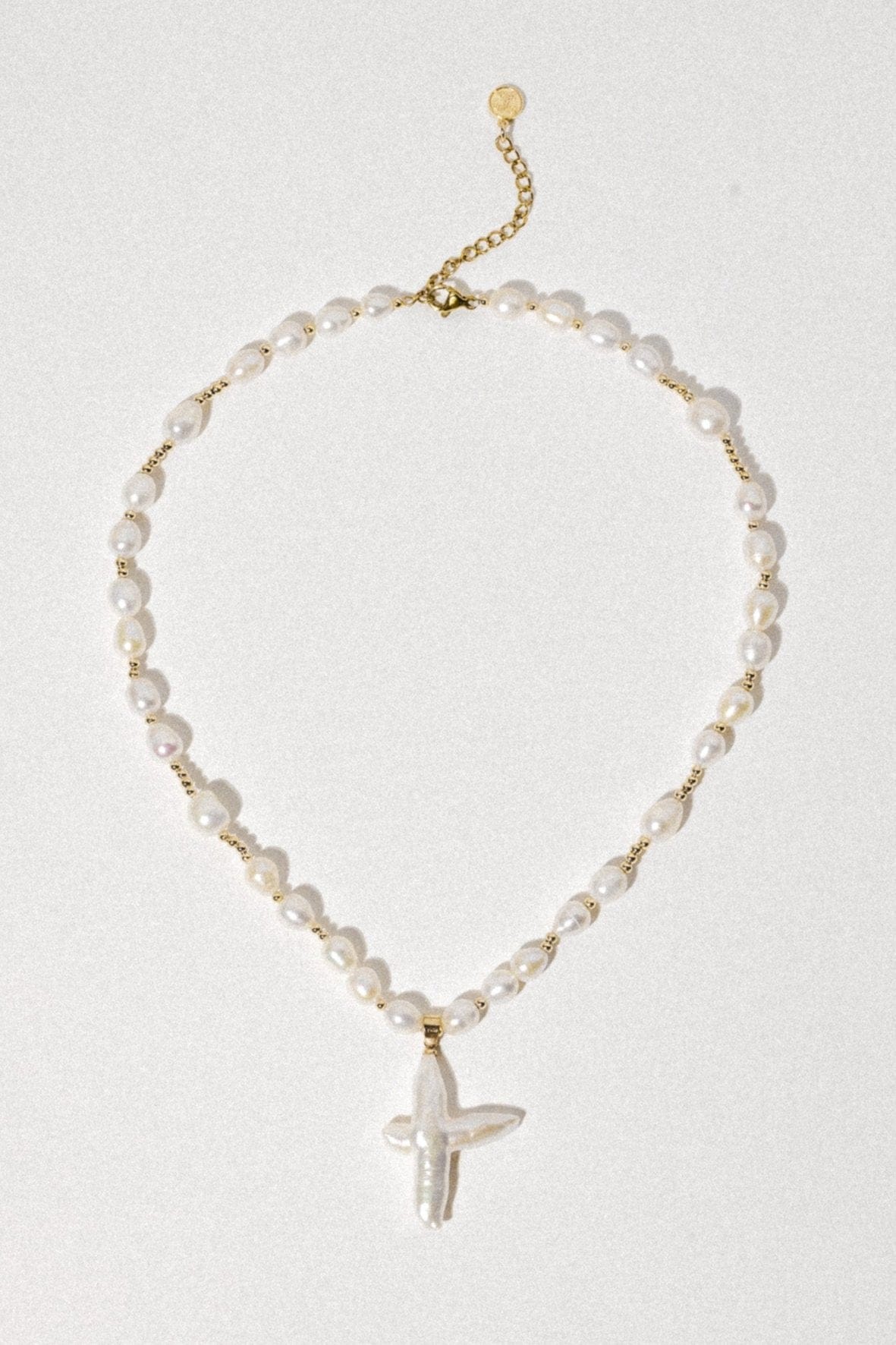 Gold-tone necklace with white pearl beads separated by gold spacers and a white cross pendant.