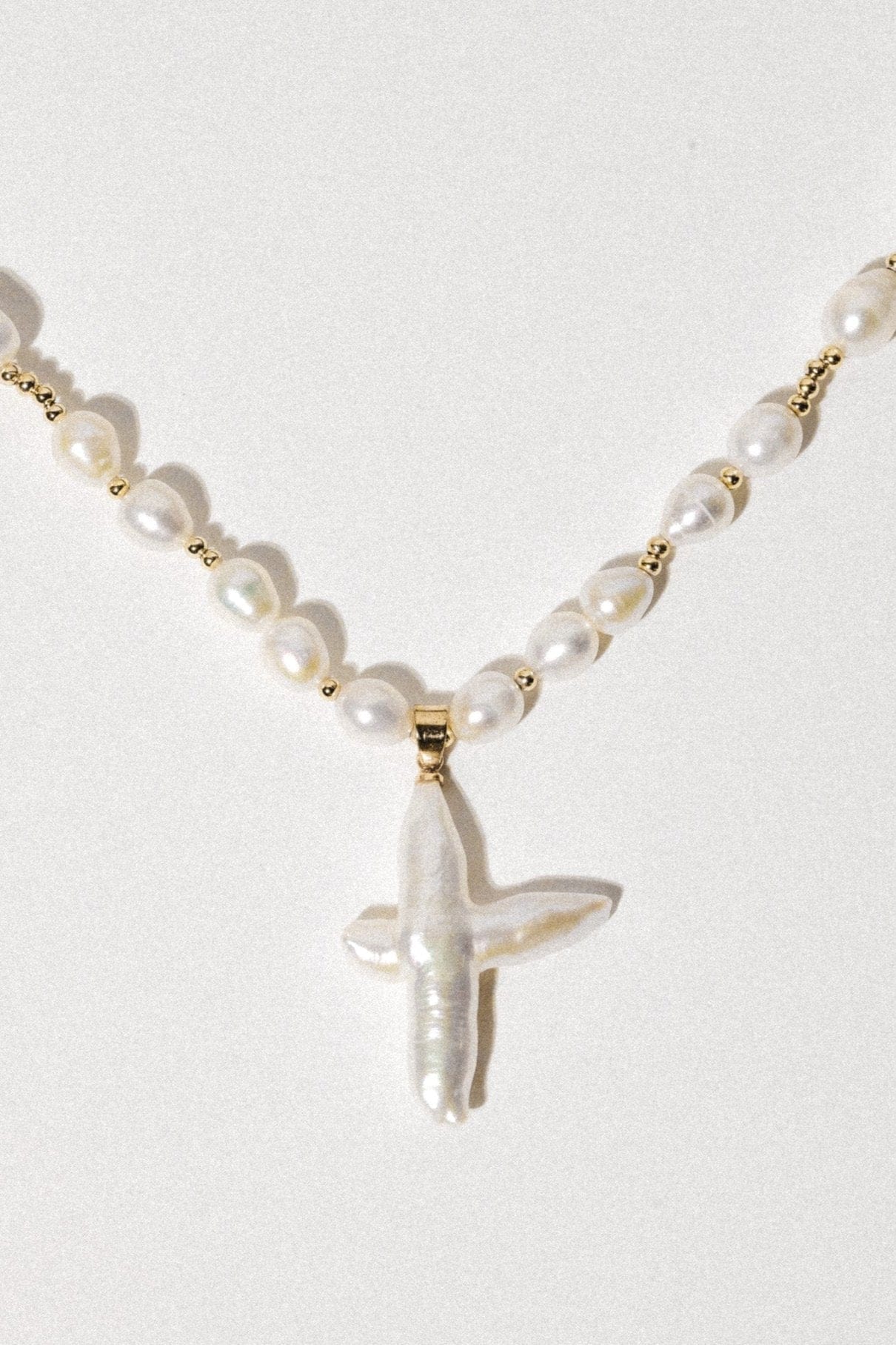 Gold-toned necklace with white pearls and a cream pearl cross pendant.