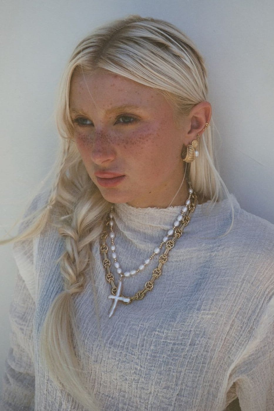 Gold chain necklace with white cross pendant and pearl beads worn layered on model.
