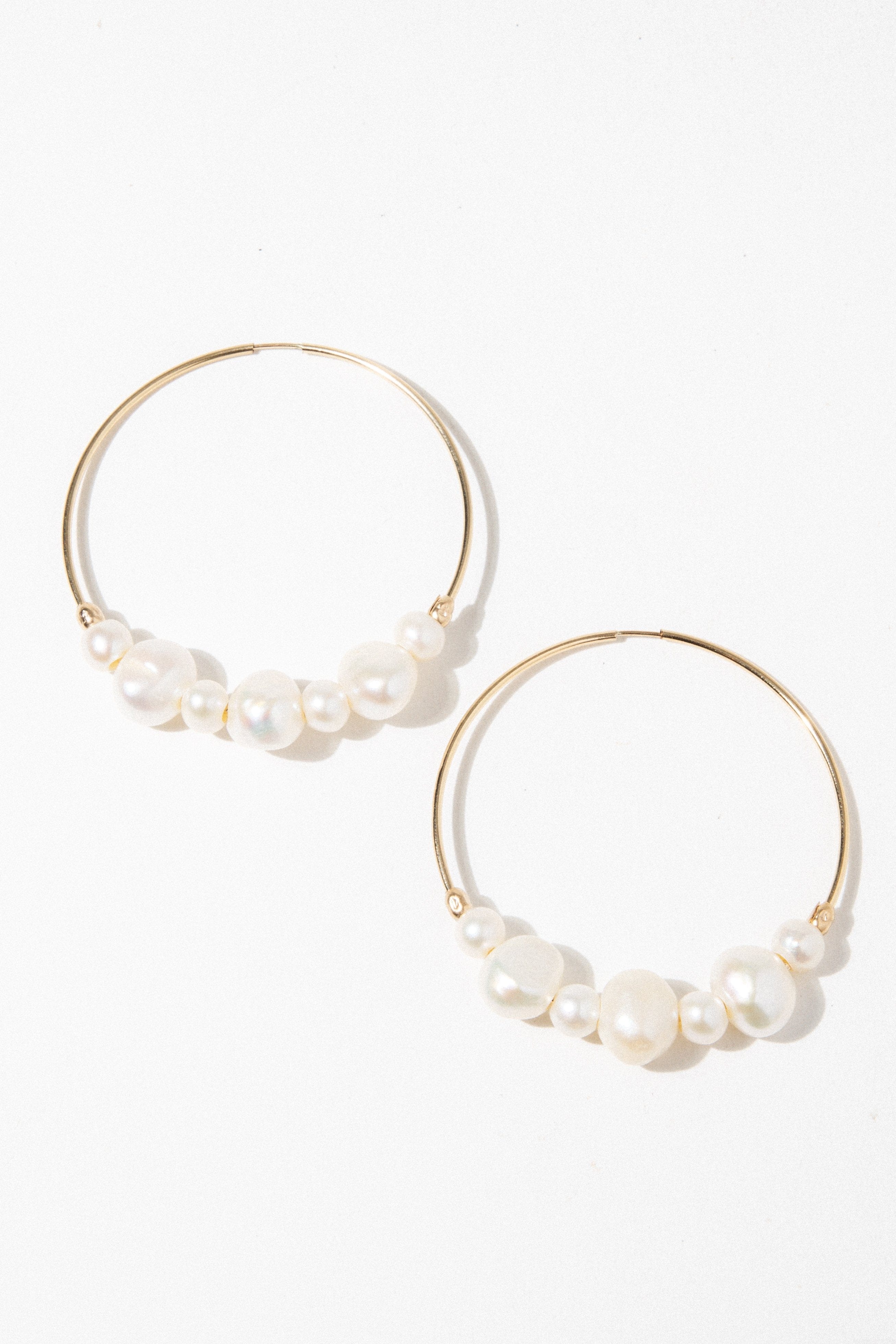 Pair of gold hoop earrings with white pearls clustered along the bottom of each hoop.