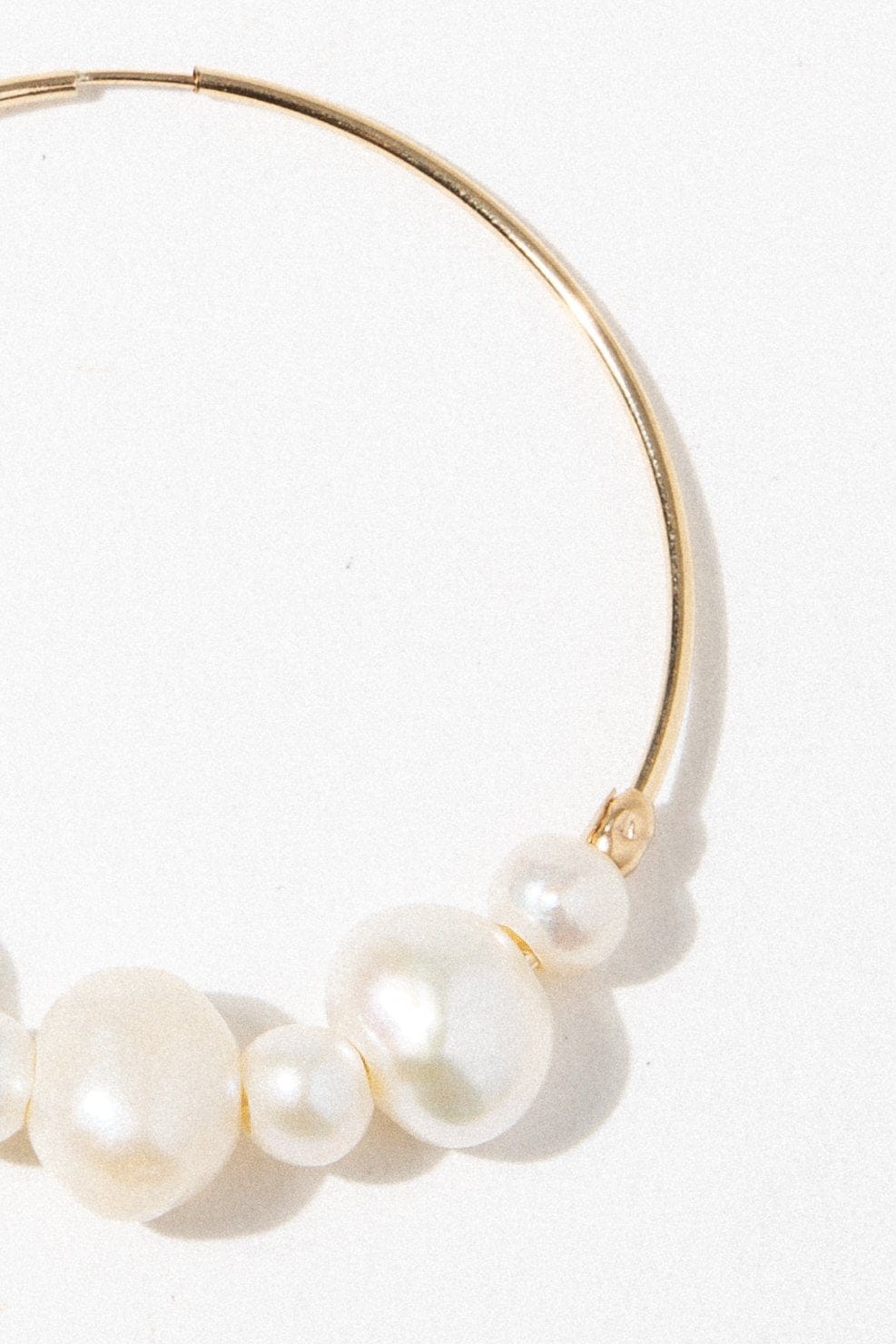 Pair of gold-toned hoop earrings with three cream pearls clustered on the curved wire.